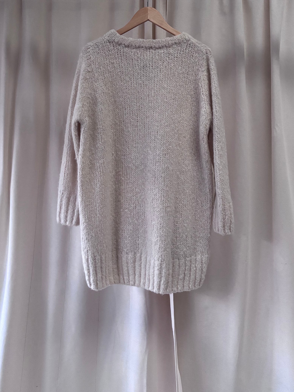 Cream knitted jumper hanging up with a cream background