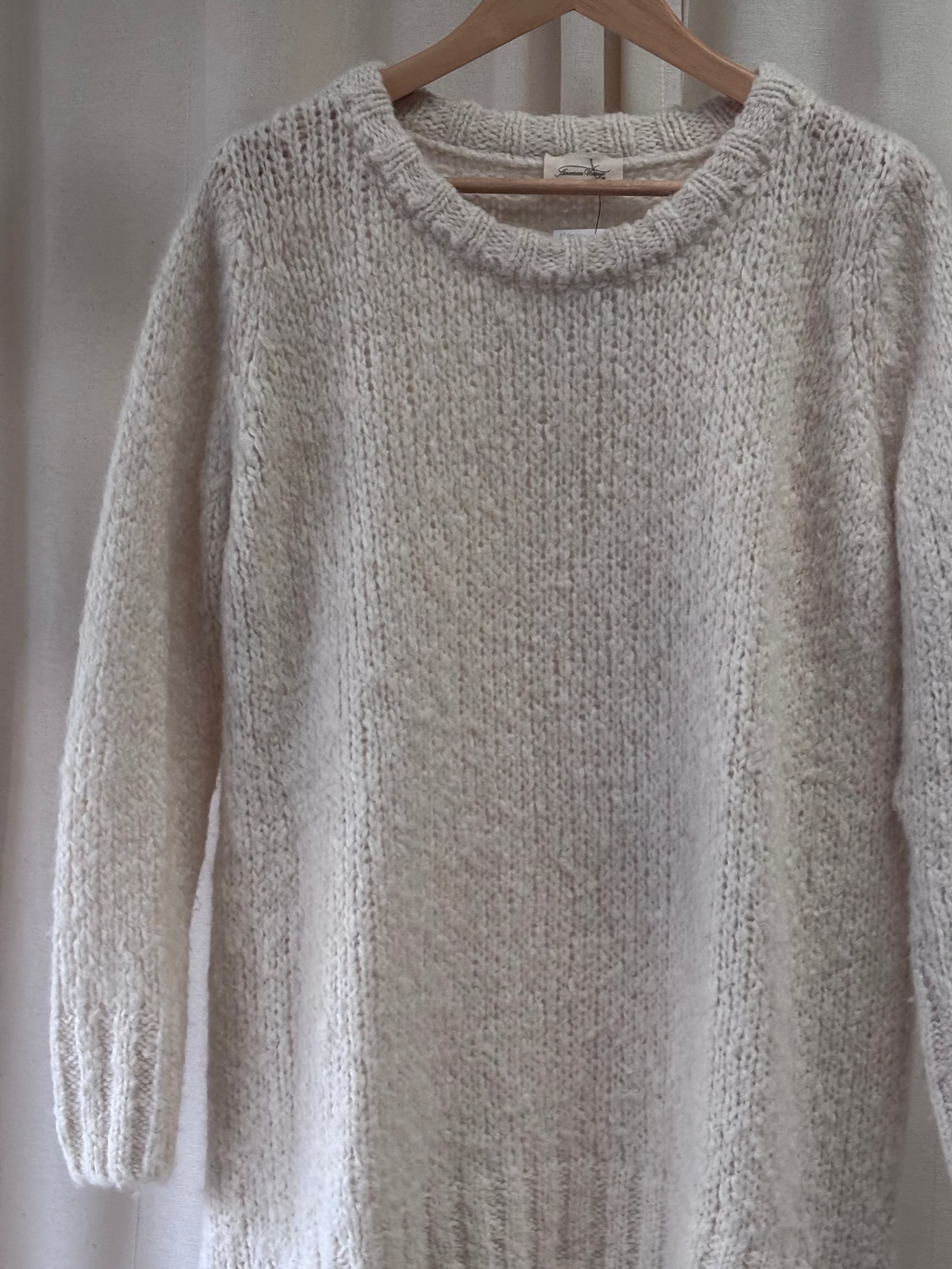 Beige knitted sweater on a wooden hanger against a neutral background