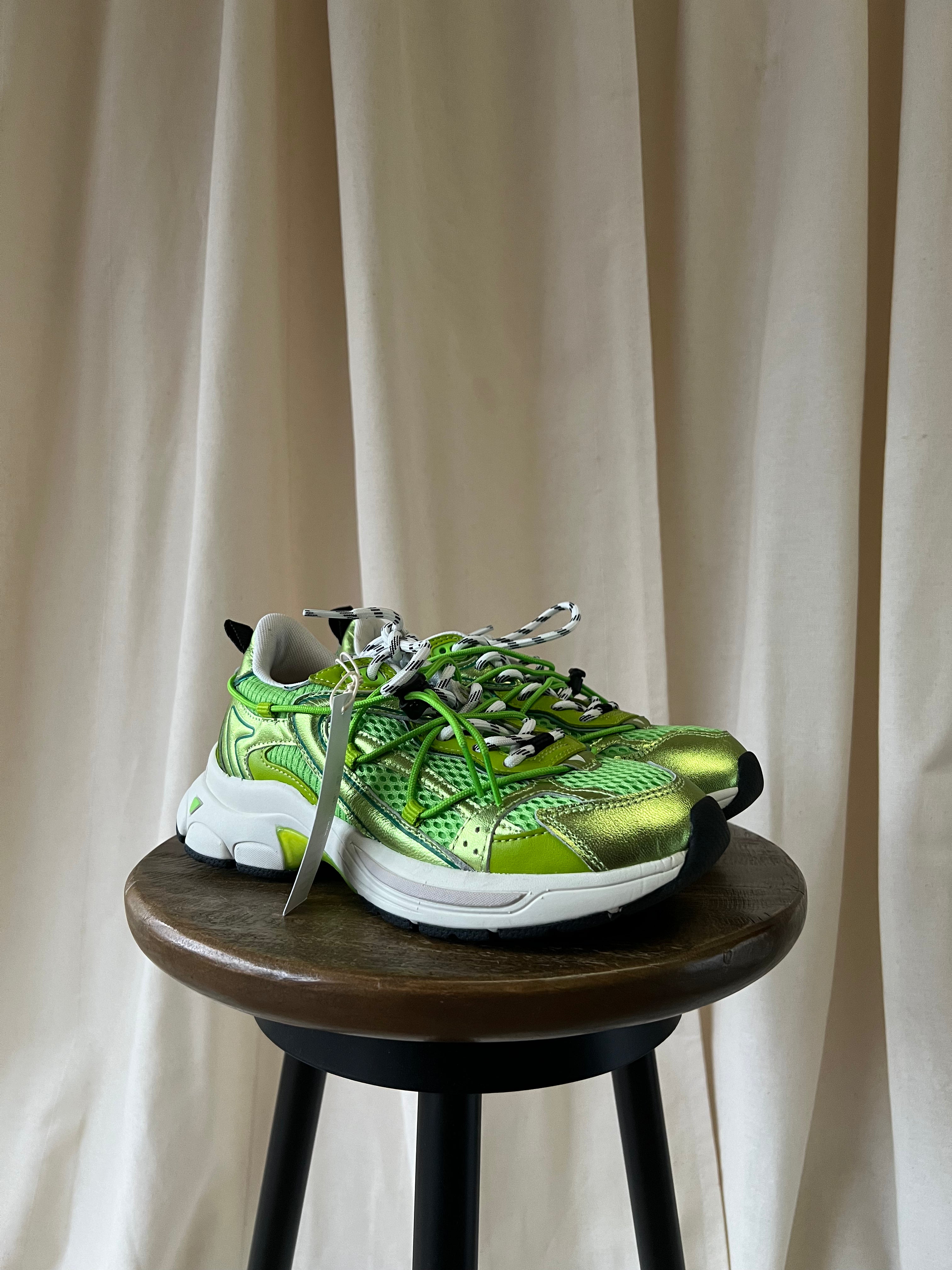 Green sneaker on a wooden stool against a beige curtain background
