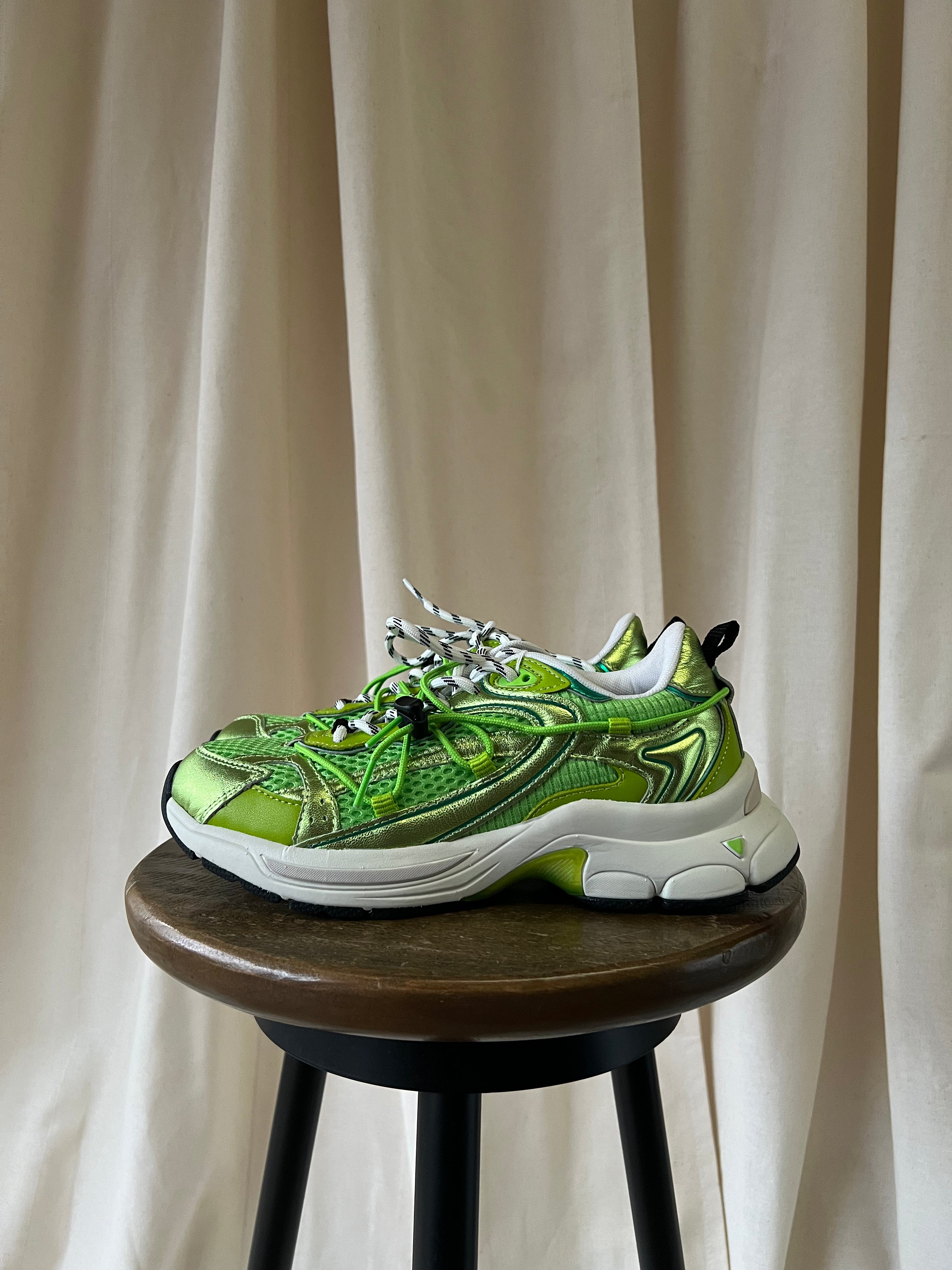 Green sneaker on a wooden stool with a beige curtain background