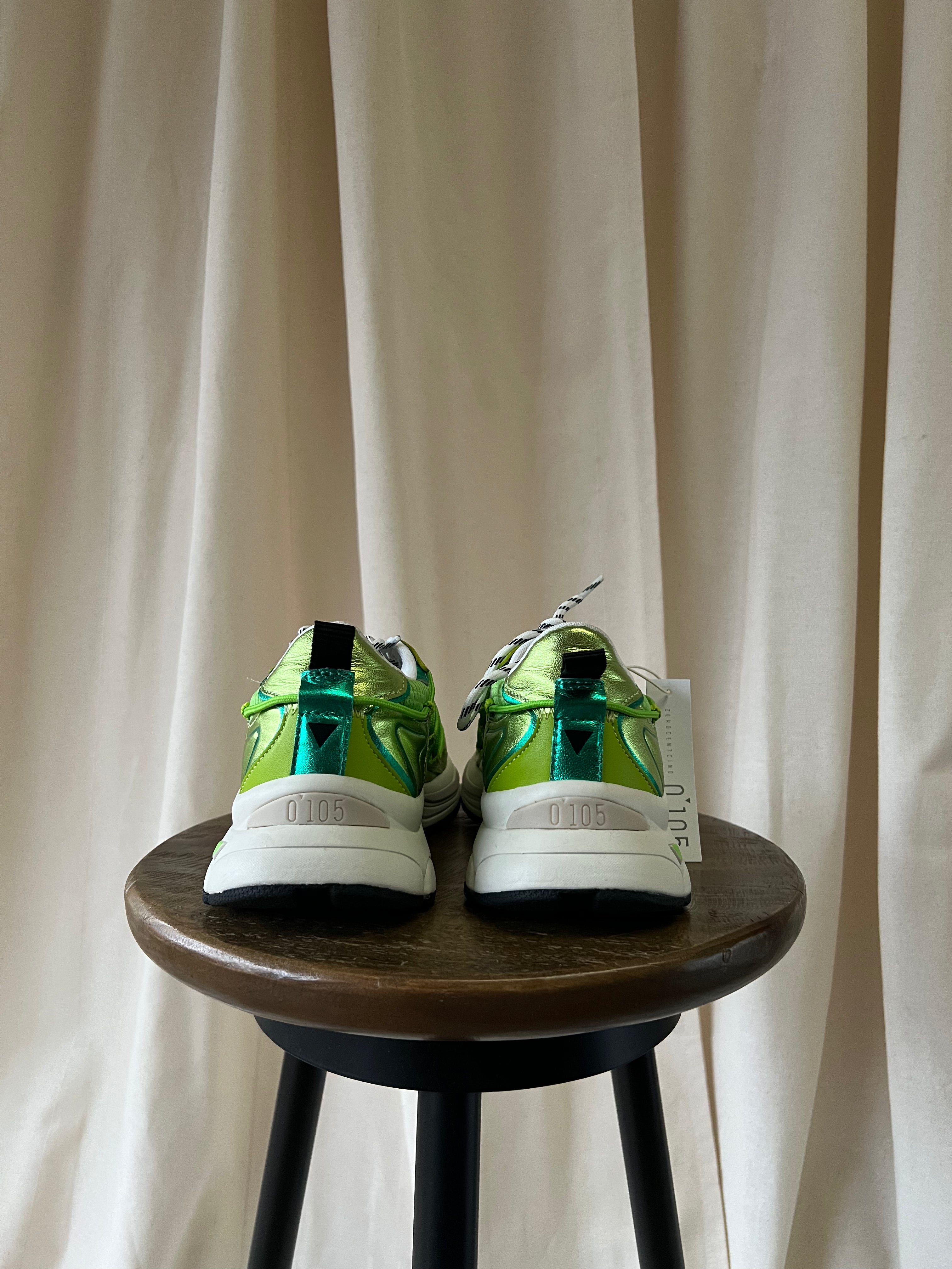 Green and white sneakers on a wooden stool with a white curtain background