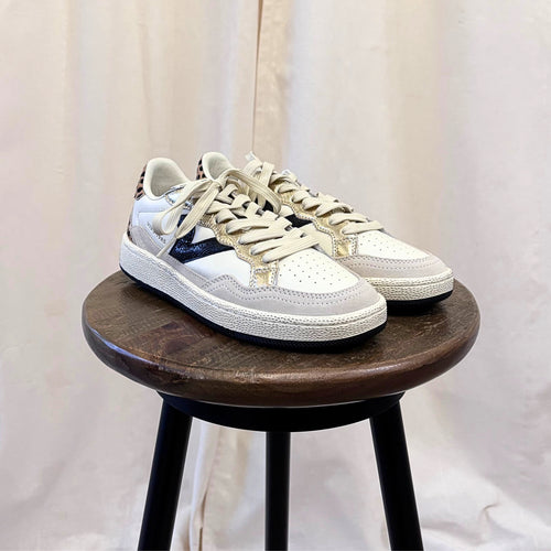 White sneakers with gold accents on a wooden stool against a white background