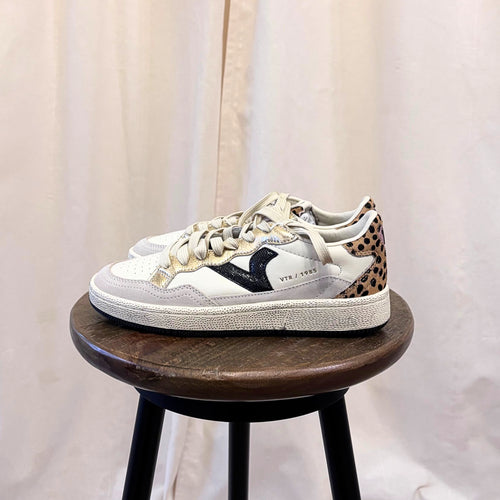 White sneaker with leopard print accents on a wooden stool against a plain background