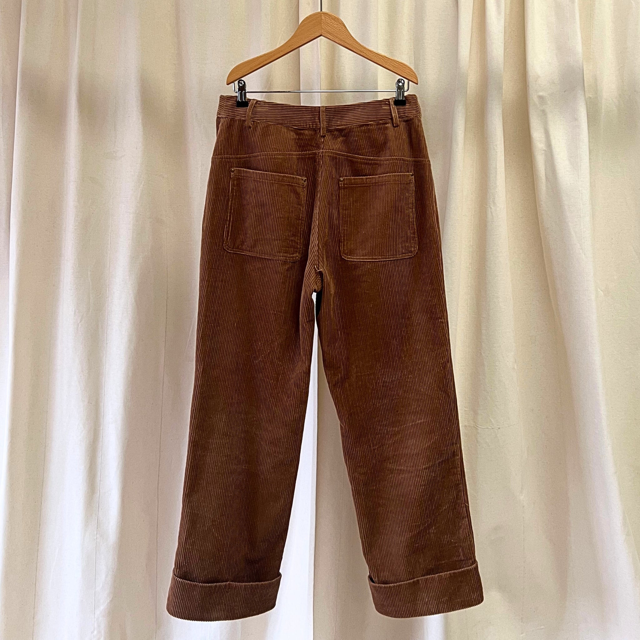 Brown corduroy pants on a wooden hanger against a beige curtain background