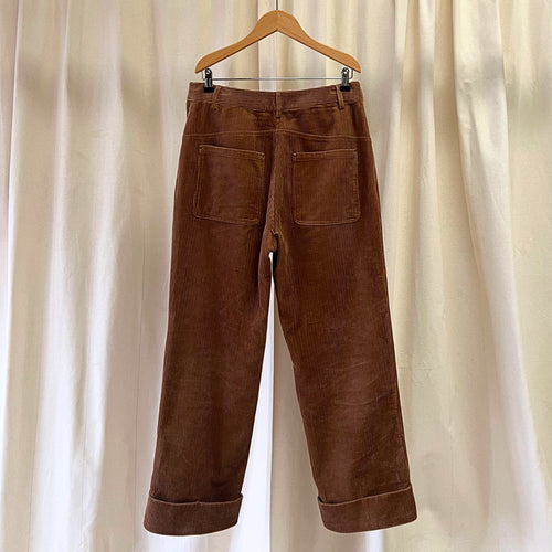 Brown corduroy pants on a wooden hanger against a beige curtain background