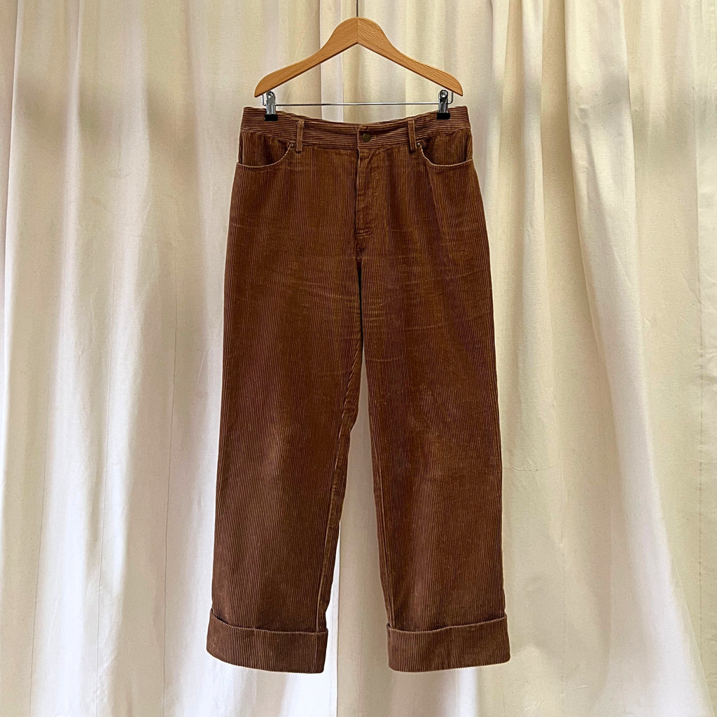 Brown corduroy pants on a wooden hanger against a beige curtain background