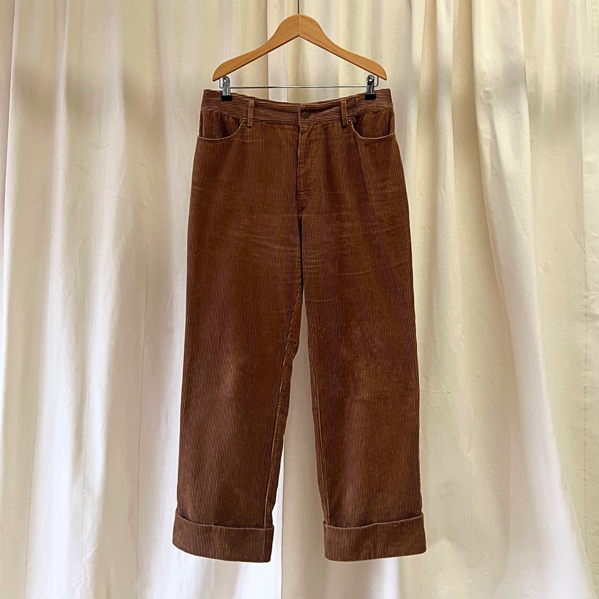 Brown corduroy pants on a wooden hanger against a beige curtain background