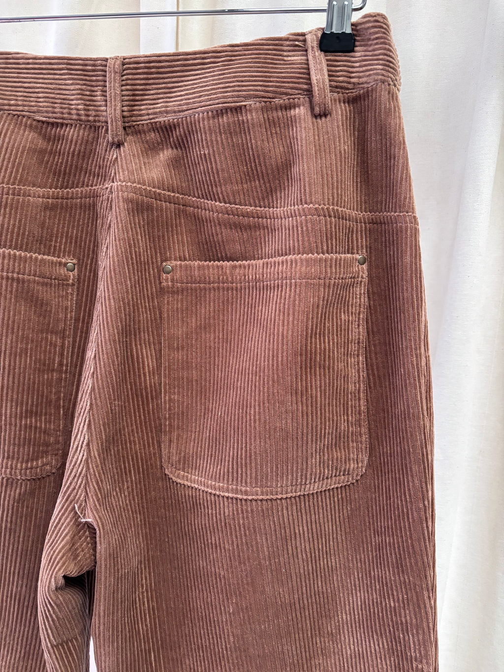 Brown corduroy pants on a hanger against a white background