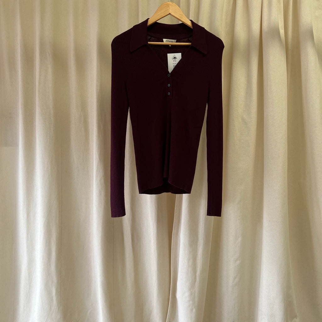 Maroon long-sleeve shirt on a hanger against a beige curtain background