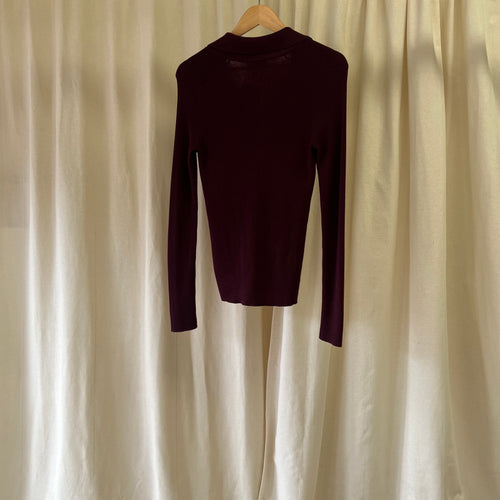Maroon long-sleeve shirt on a hanger against a beige curtain background