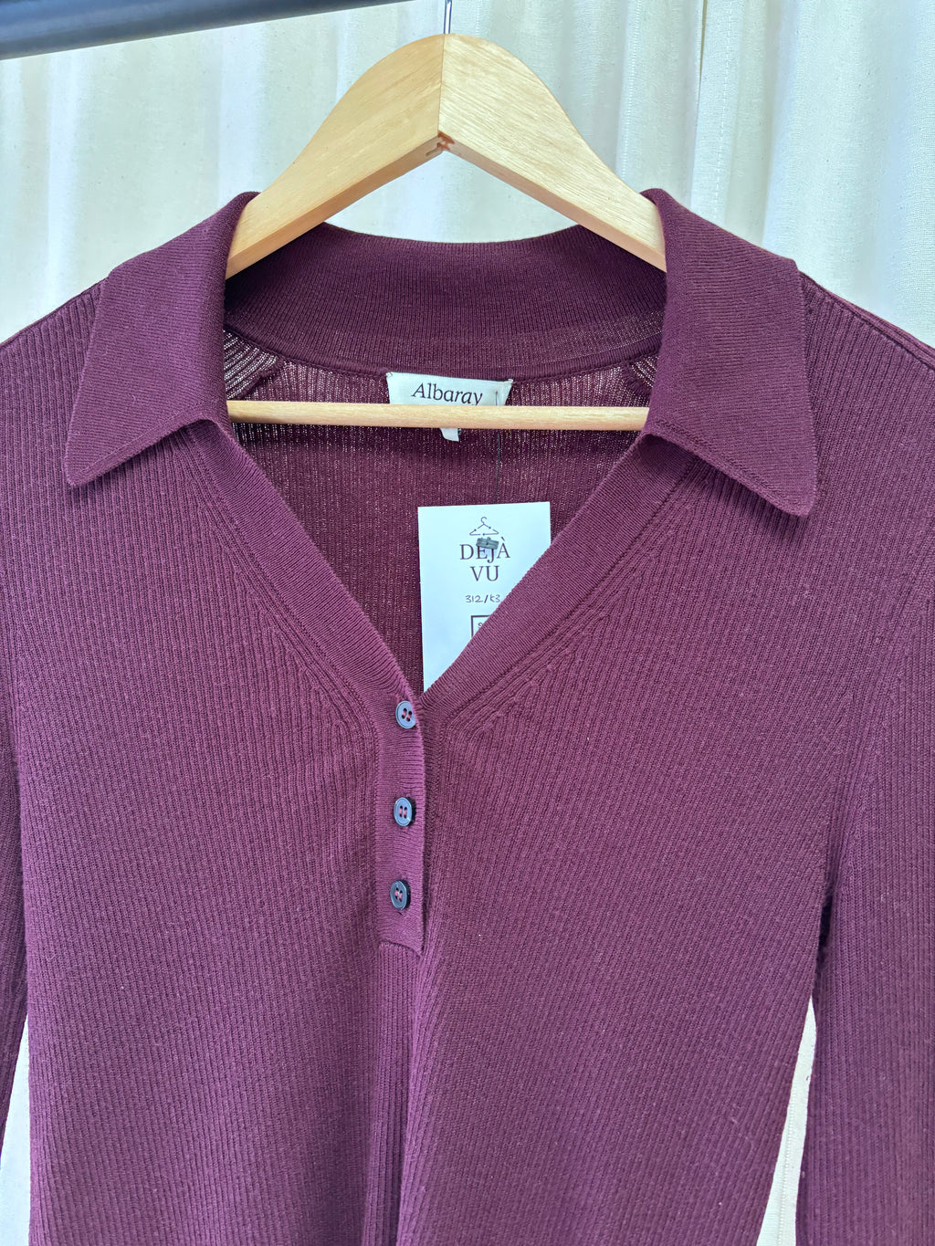 Maroon red jumper on a hanger with a visible brand label against a neutral background