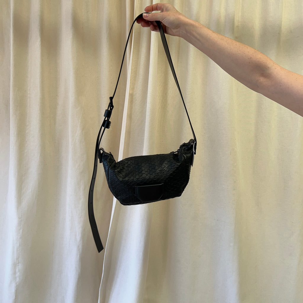 Black handbag held by a hand against a plain background