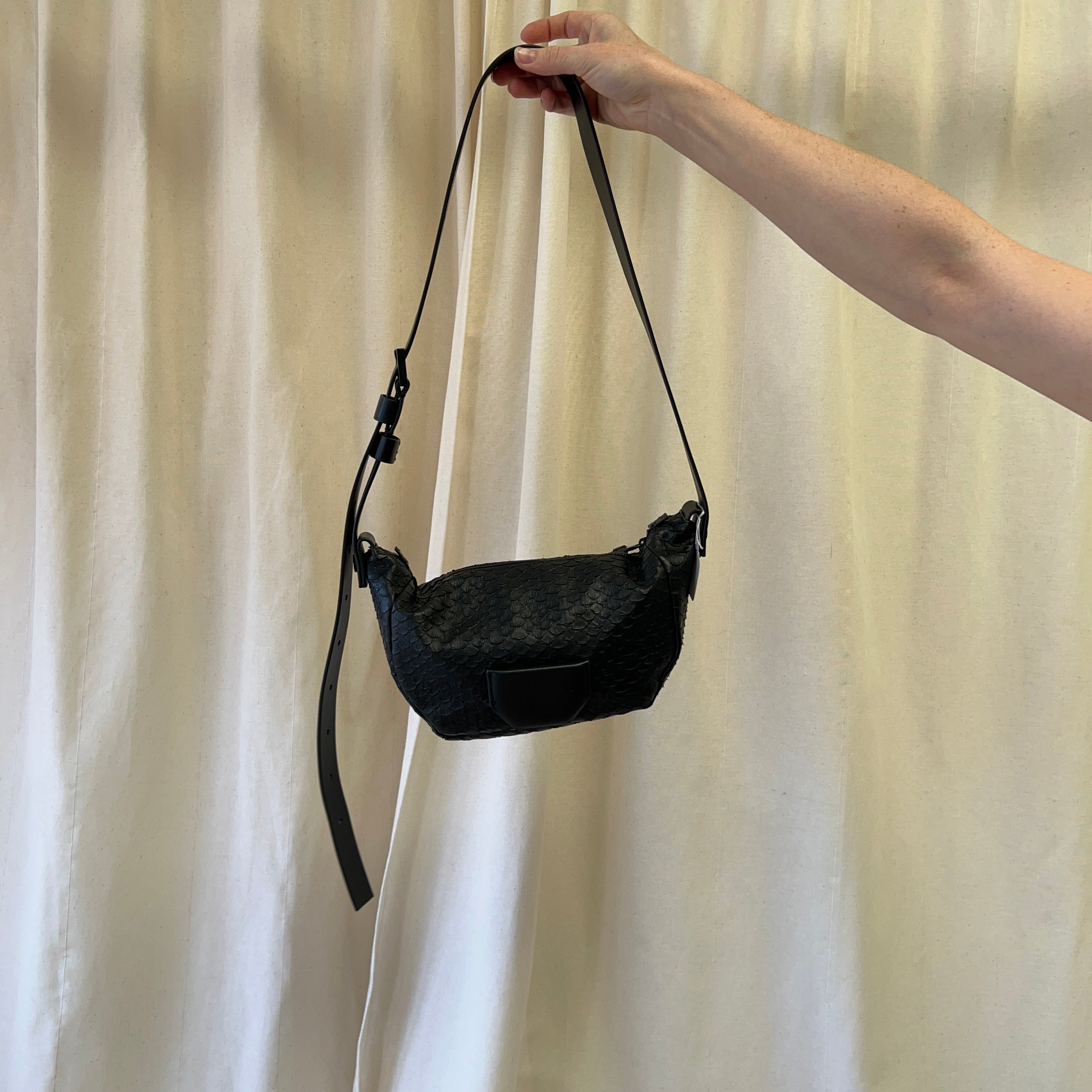 Black handbag held by a hand against a plain background