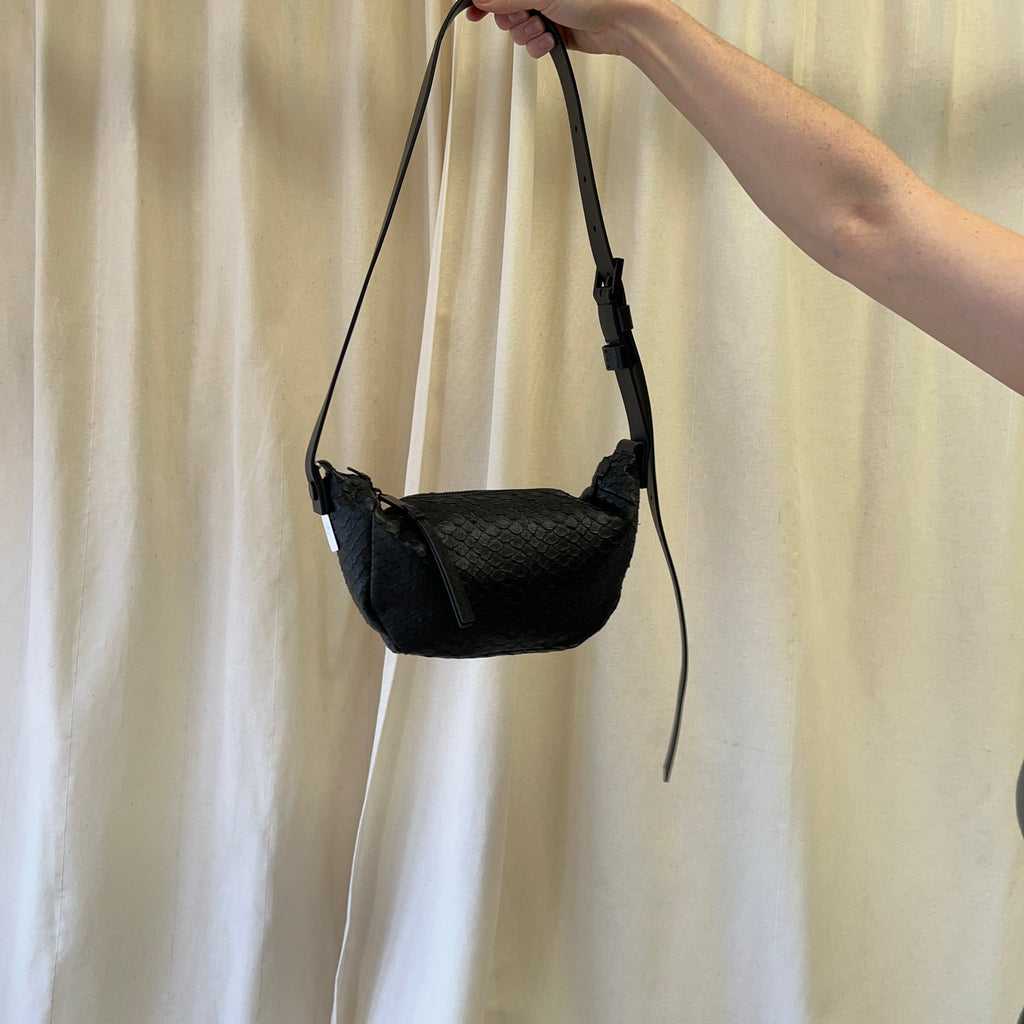 Black woven handbag held by a person against a beige curtain background