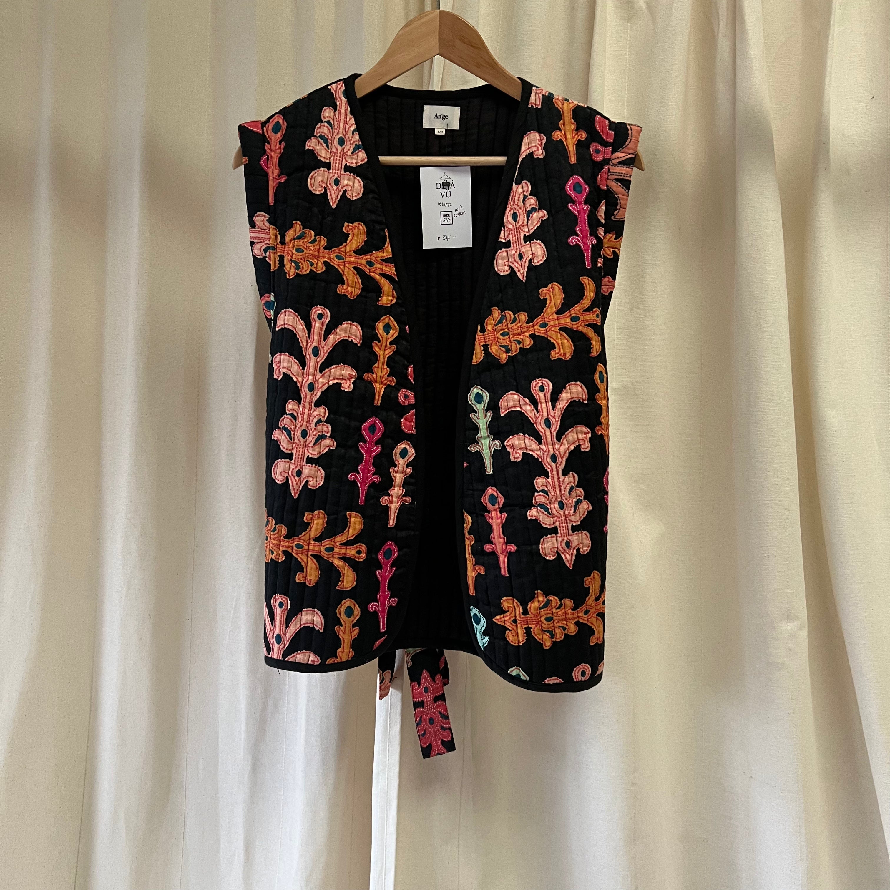 Embroidered vest with colorful patterns on a hanger against a white curtain background