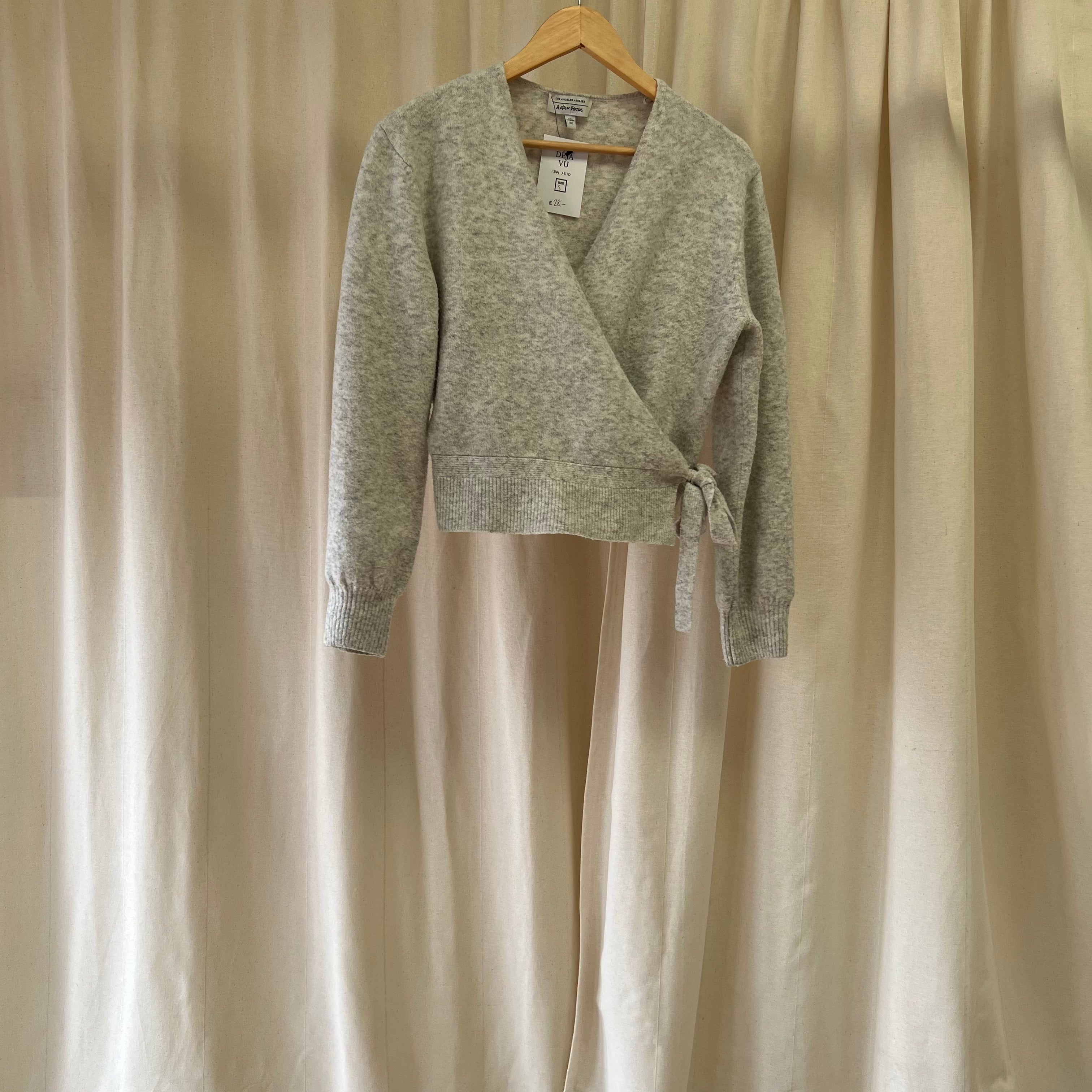 Gray wrap jumper on a hanger against a beige curtain background