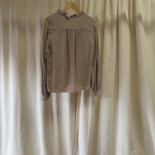 Brown patterned blouse on a hanger against a beige curtain background