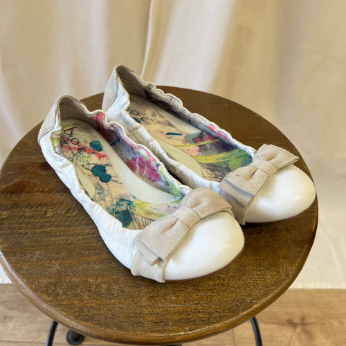 Pair of white shoes with colorful designs on a wooden stool.