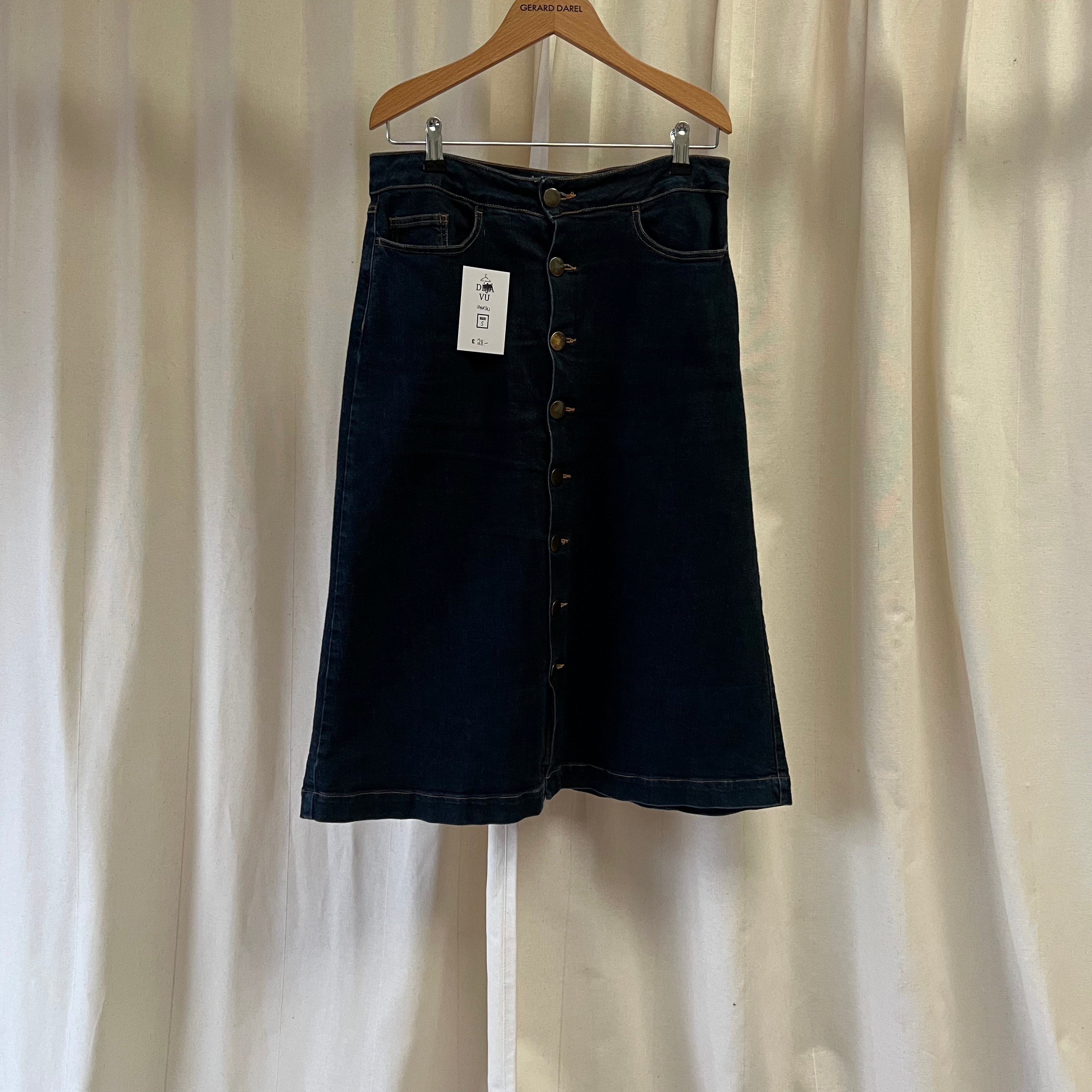 Black denim skirt on a hanger against a white curtain background