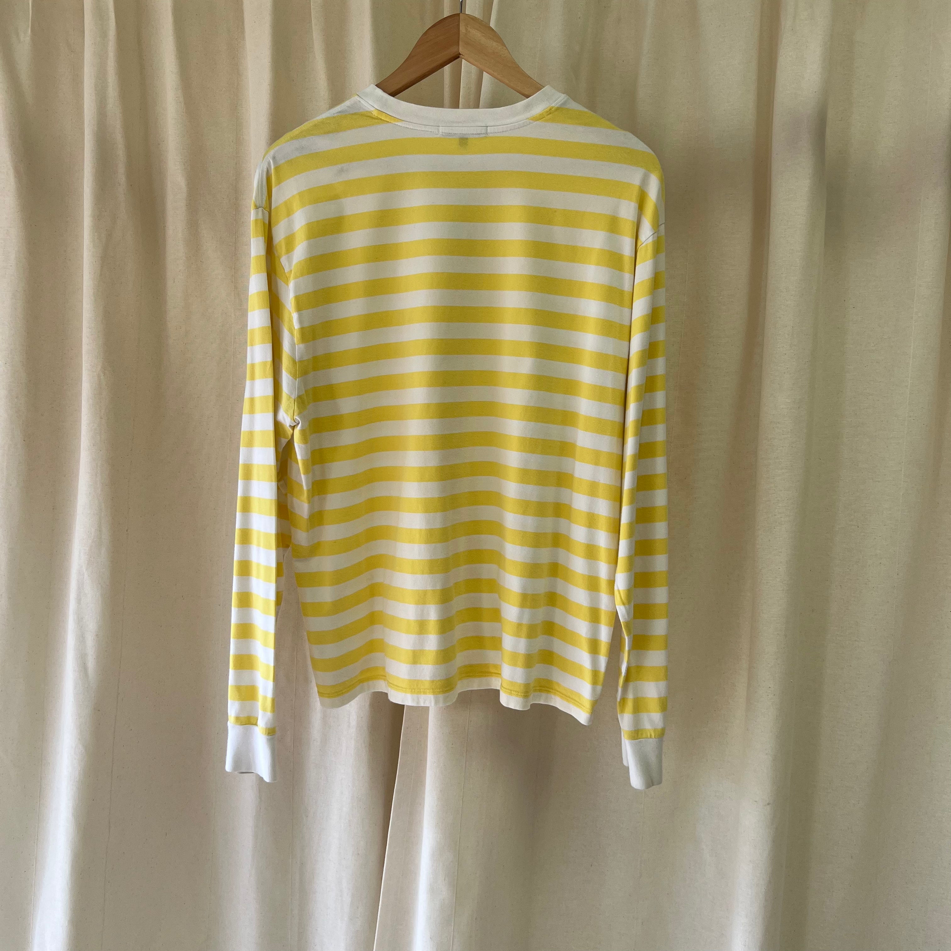 Yellow and white striped long-sleeve shirt on a wooden hanger against a beige curtain background