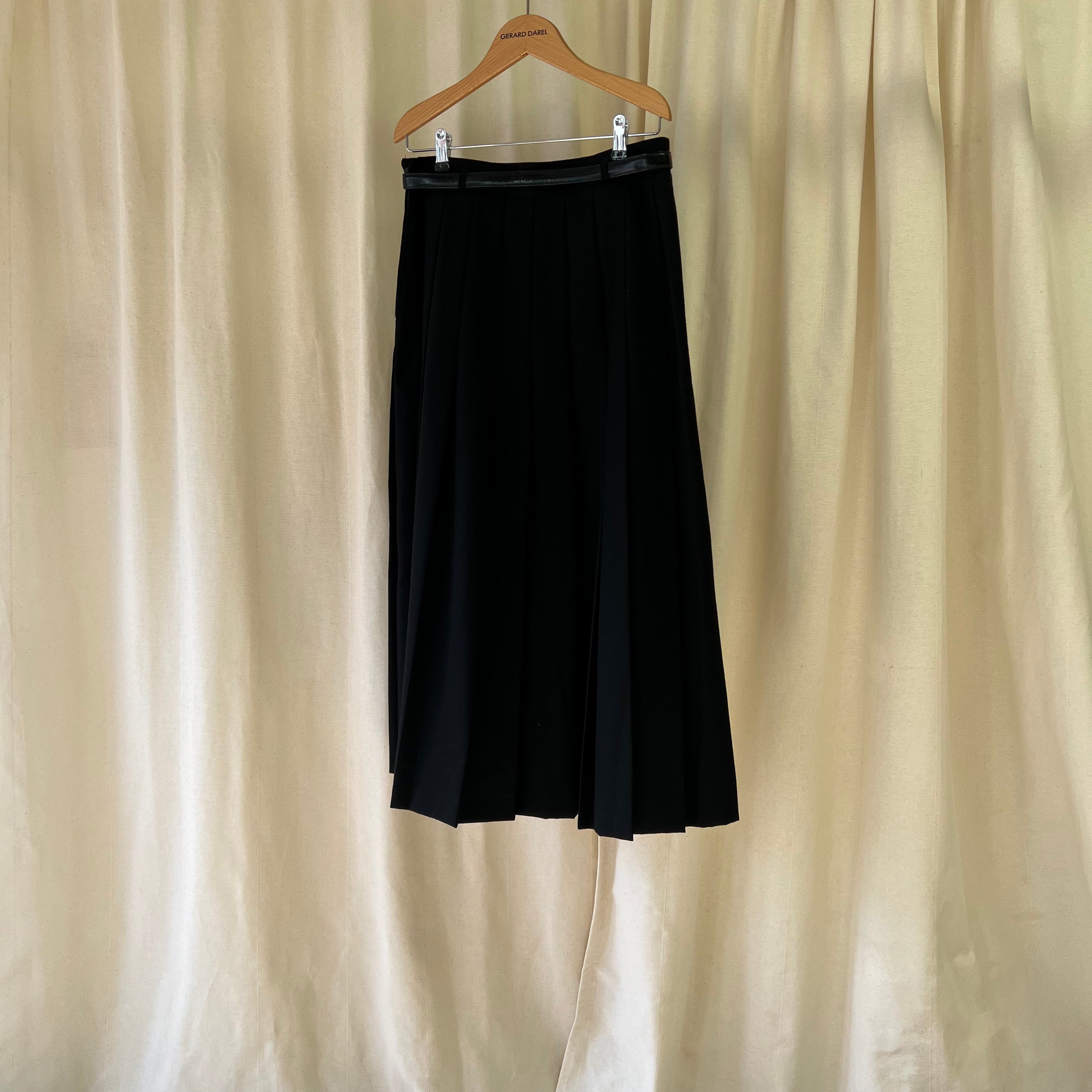 Black skirt on a hanger against a beige curtain background