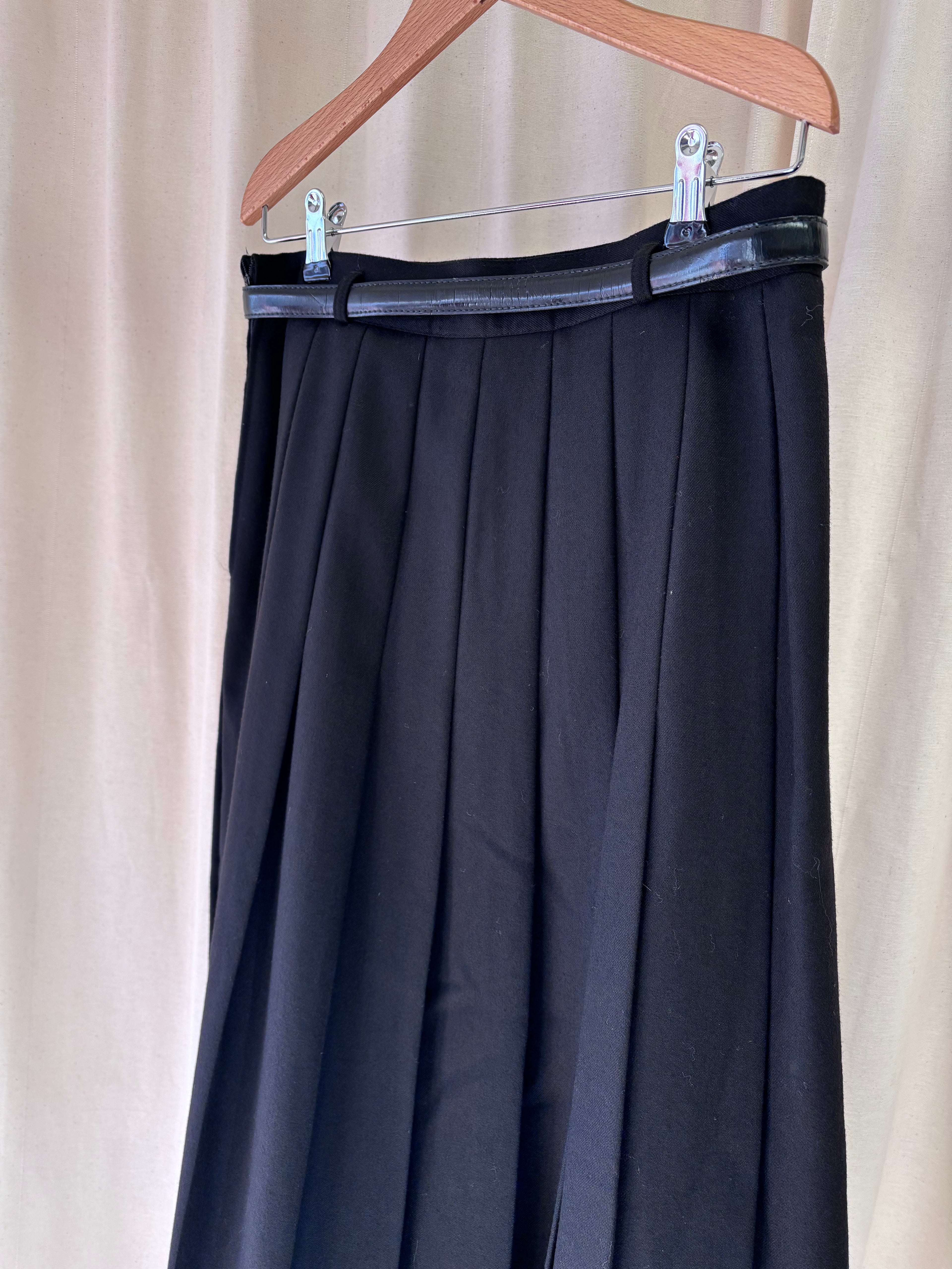 Black pleated skirt on a hanger against a beige curtain background