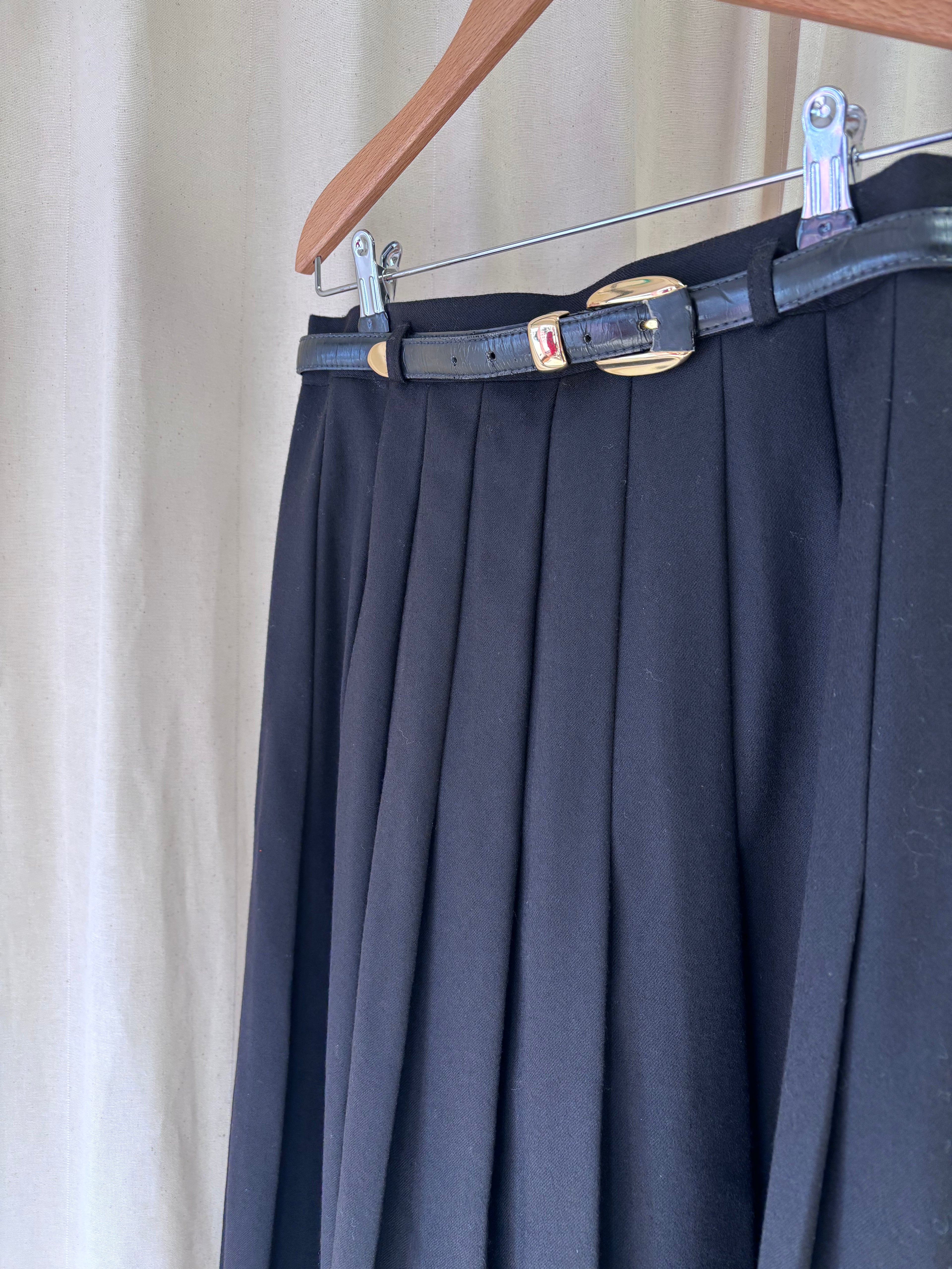 Black pleated skirt with a belt on a hanger against a neutral background