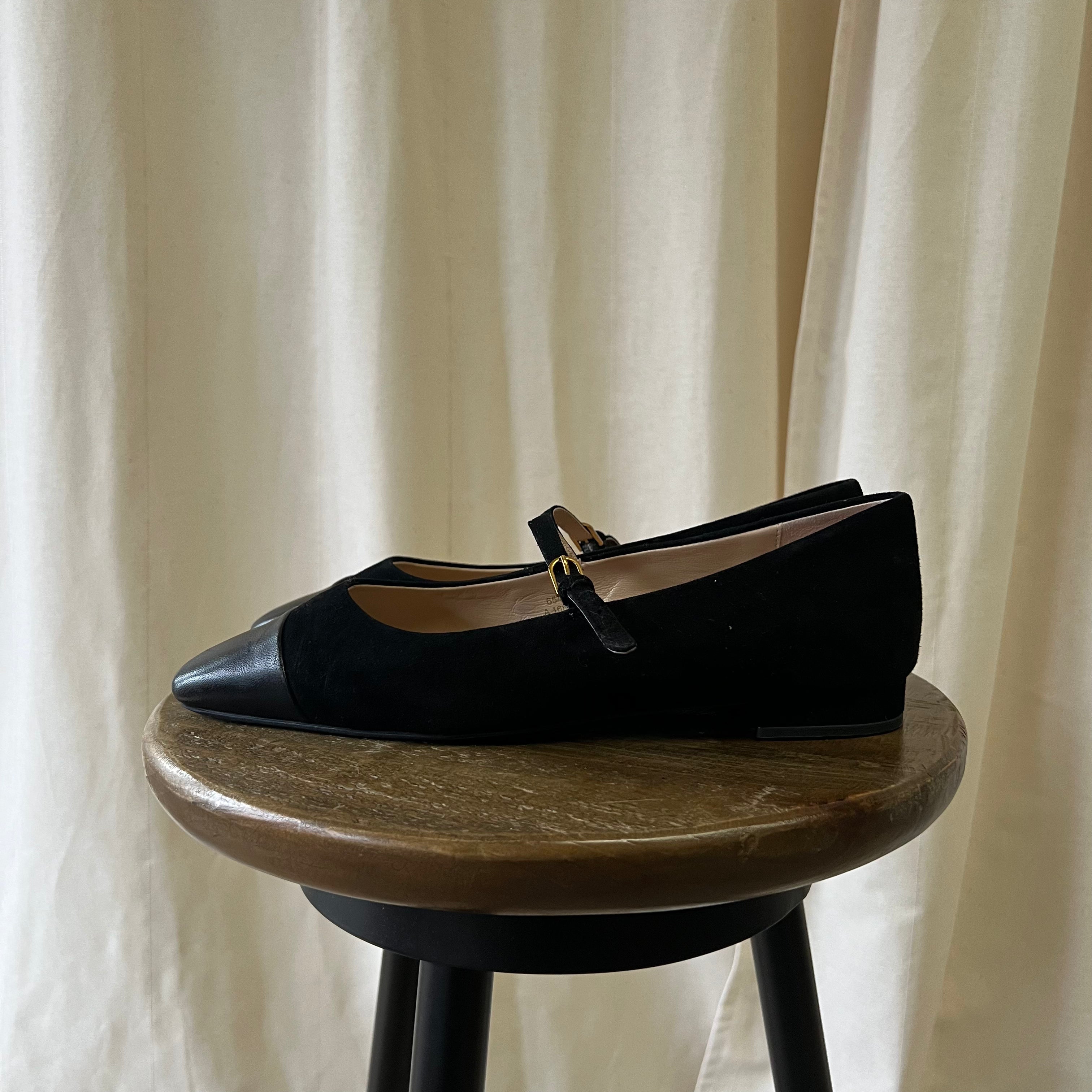 Black shoe on a wooden stool with a beige curtain background