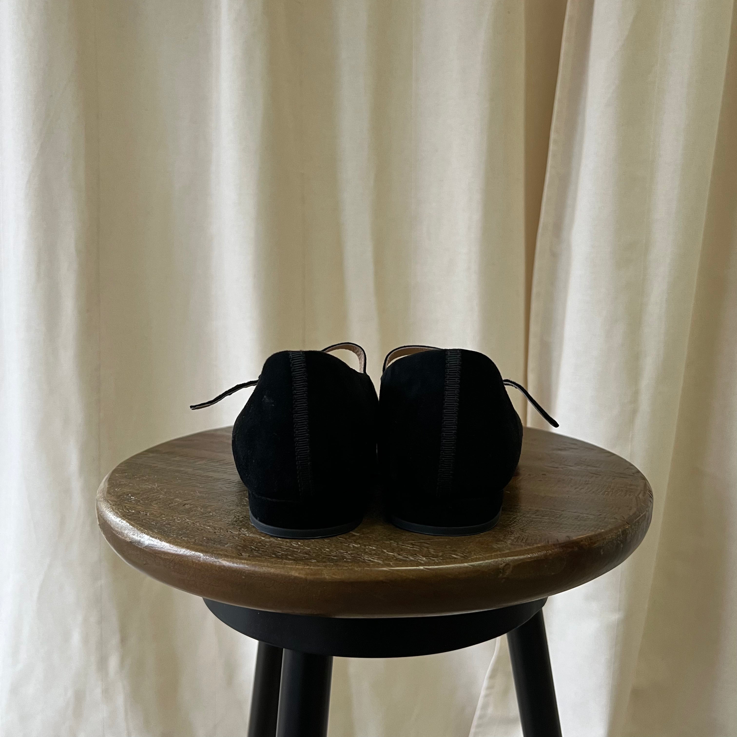 Black shoes on a wooden stool with a neutral curtain background