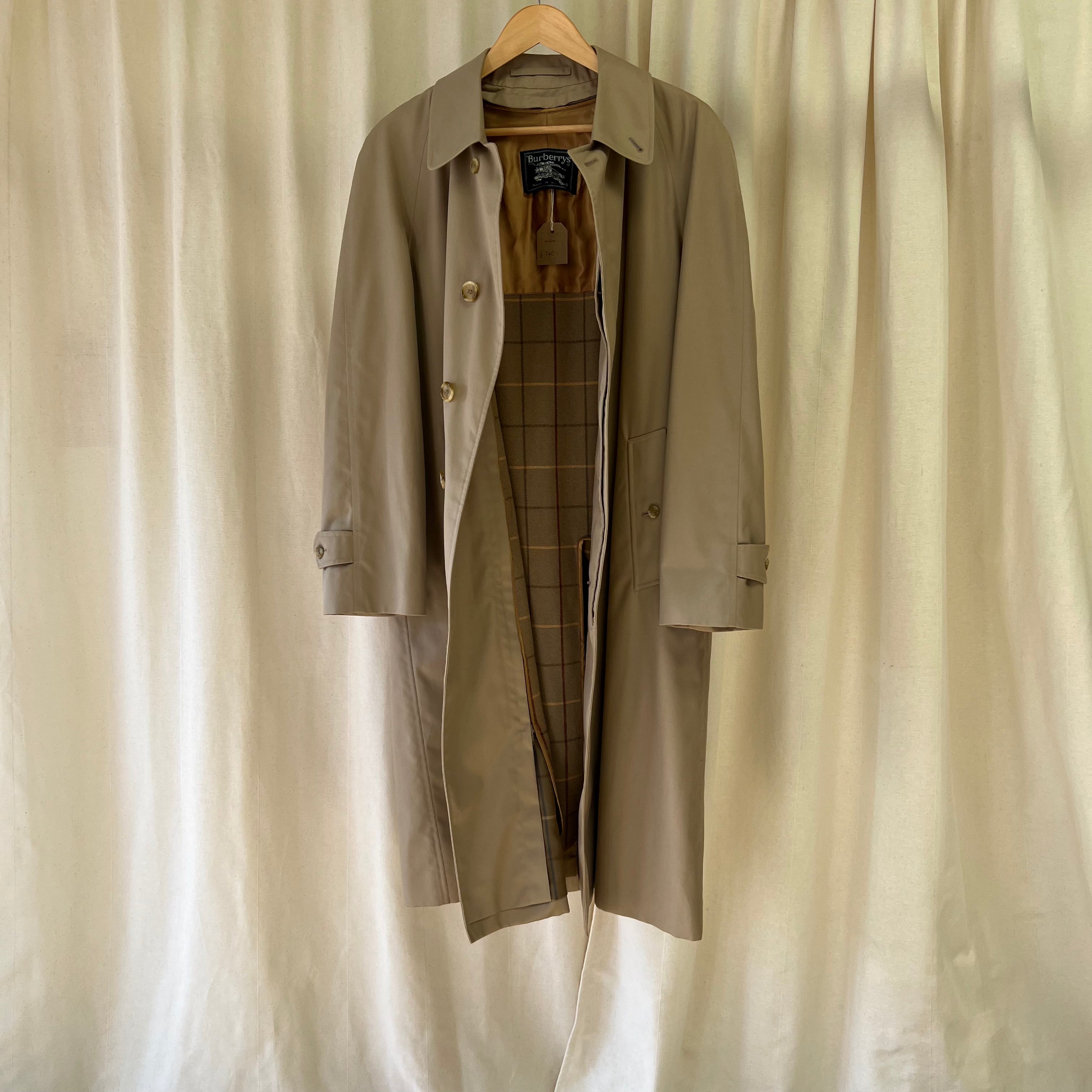 Trench coat and plaid pants on a hanger against a beige curtain background