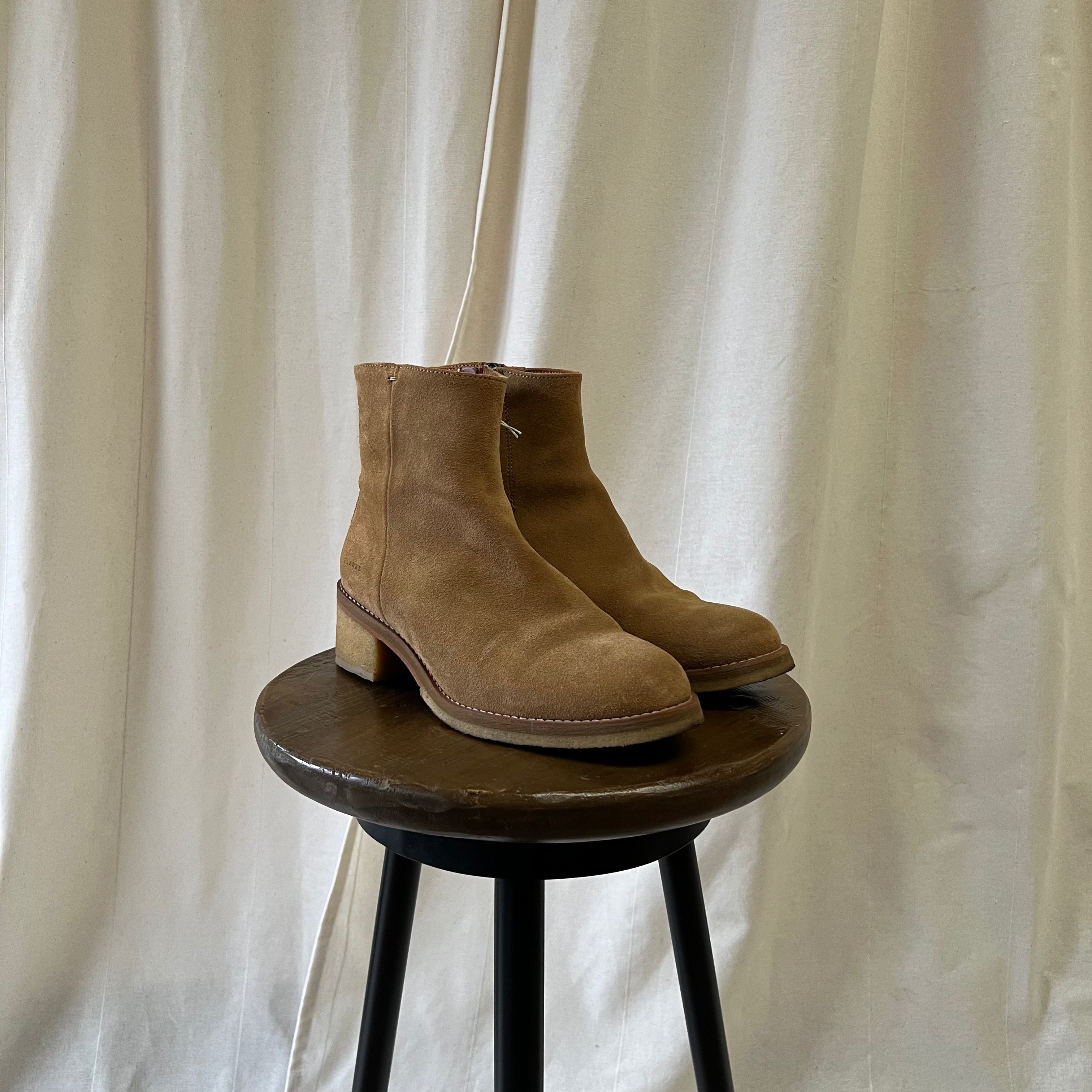 Pair of brown suede boots on a wooden stool against a white curtain background