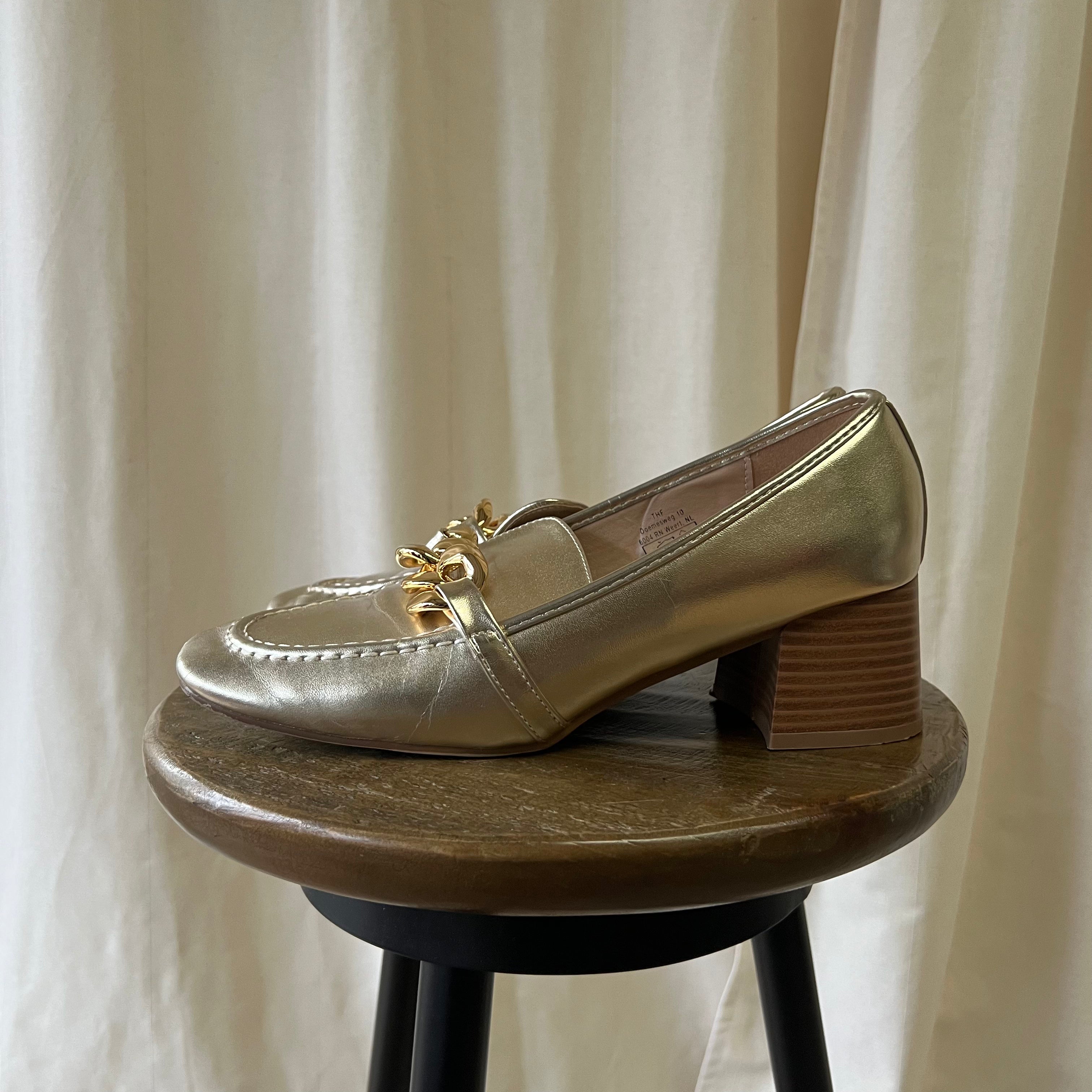 Gold loafer shoe on a wooden stool with a neutral curtain background