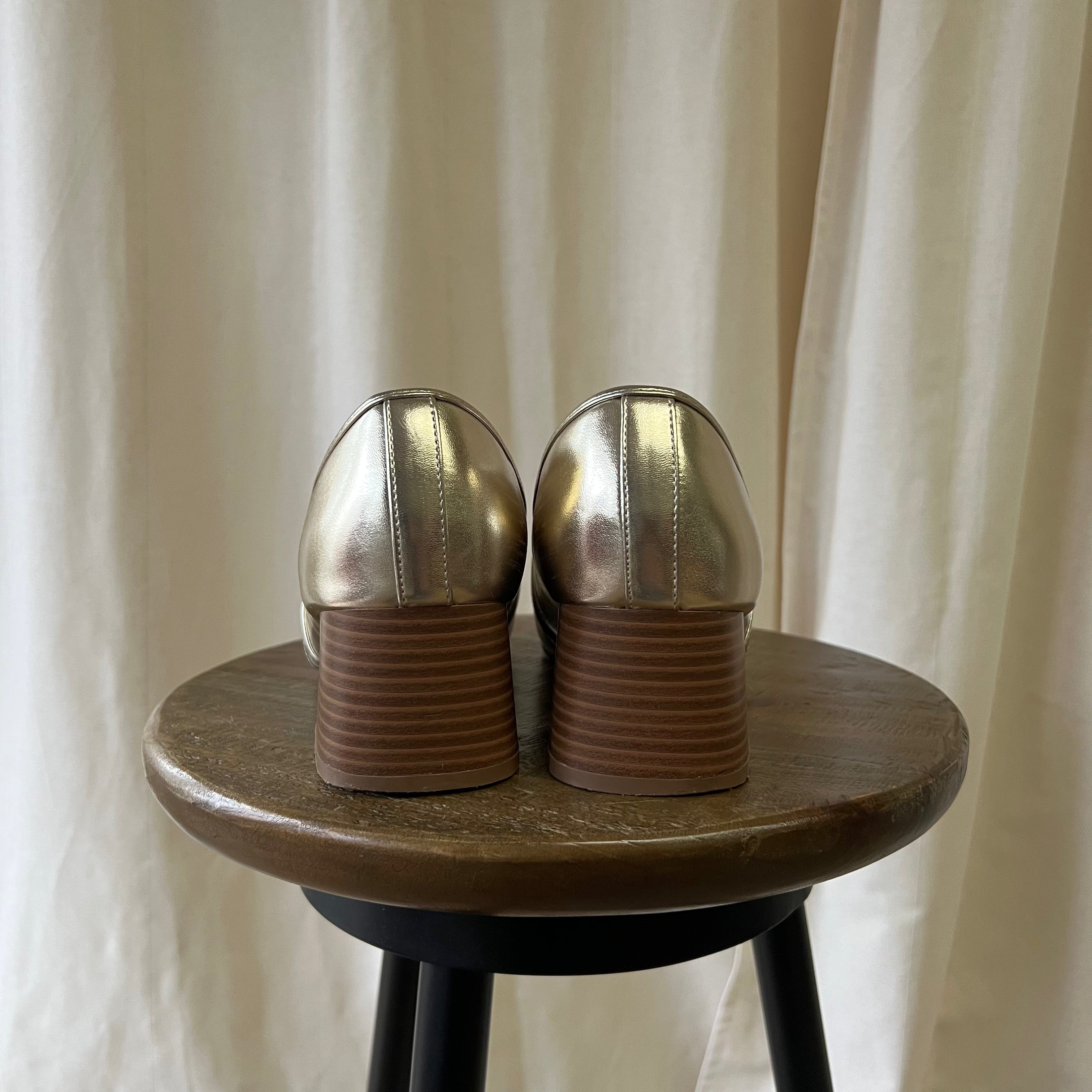 Pair of metallic shoes on a wooden stool with a neutral curtain background