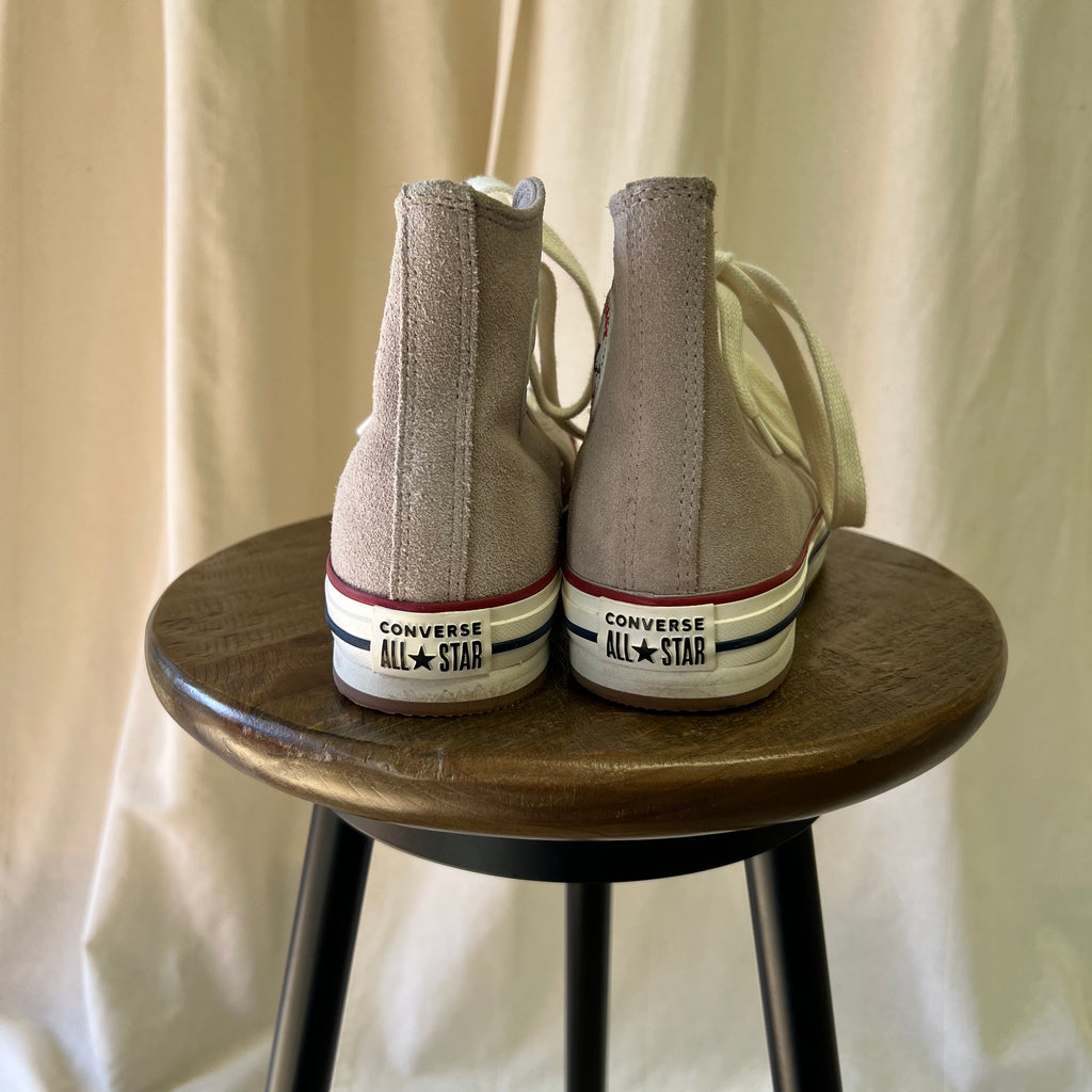 Pair of beige Converse All Star shoes on a wooden stool with a plain background