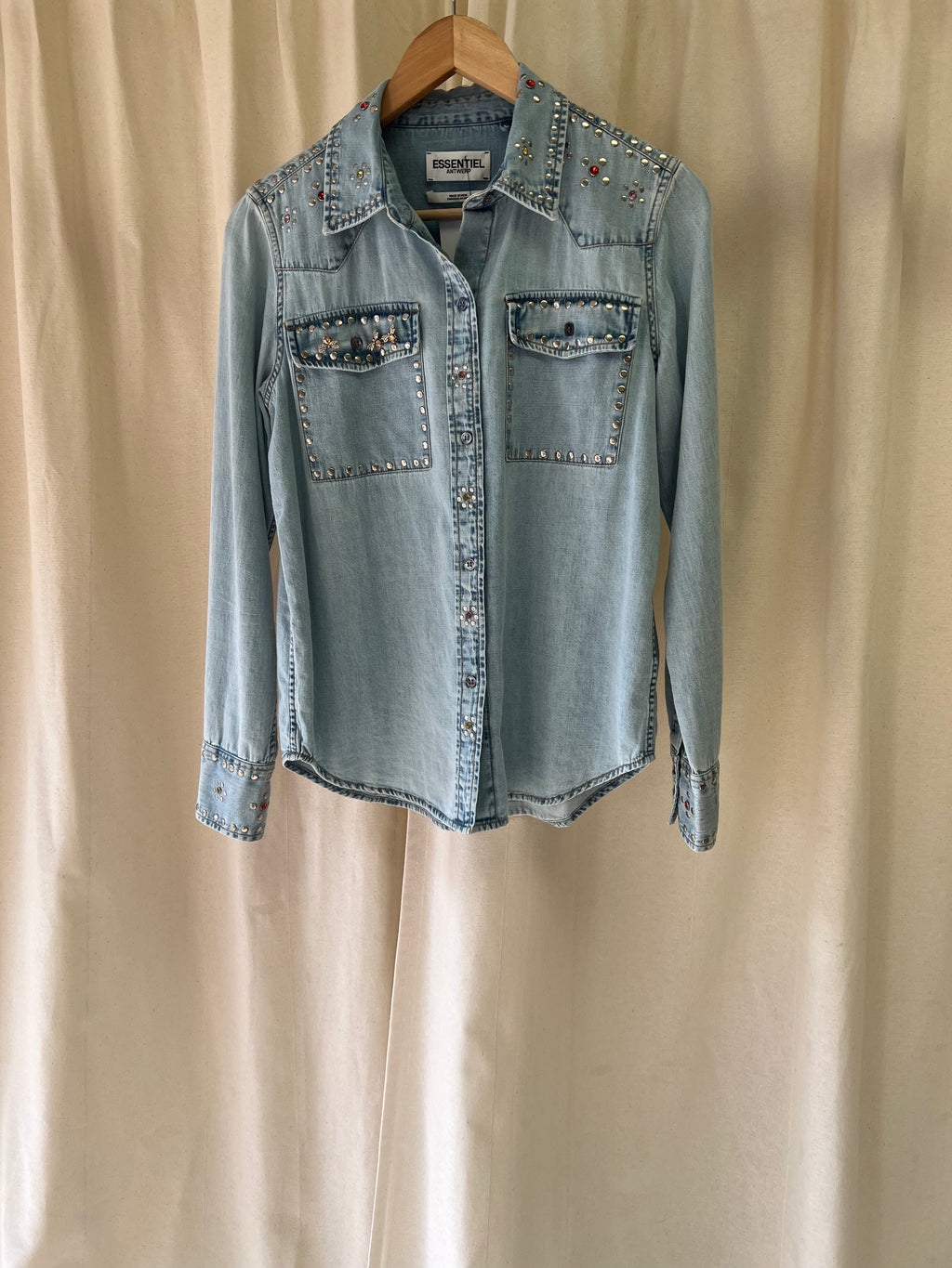 Light blue denim shirt with embellishments on a beige background
