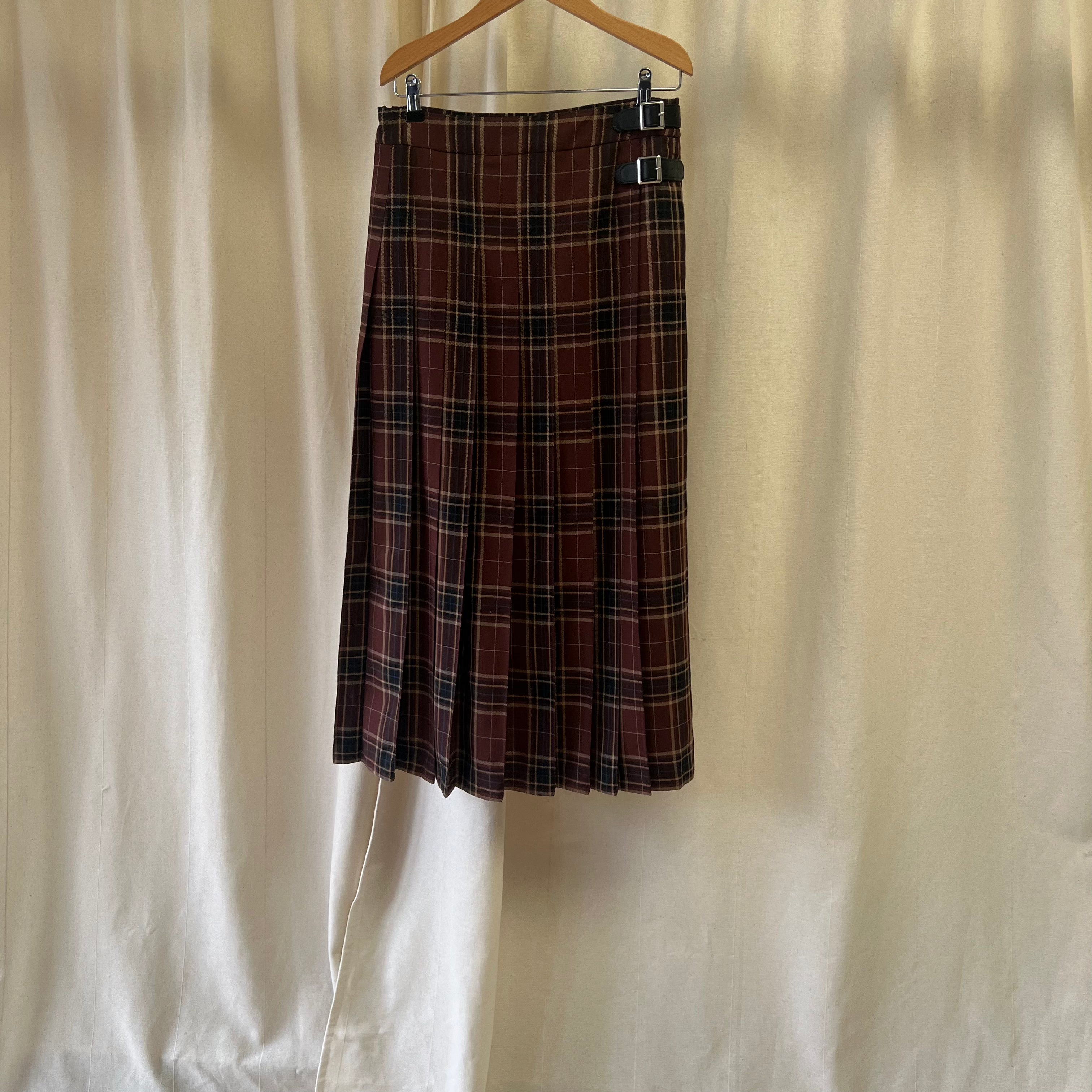 Plaid skirt hanging on a wooden hanger against a plain background