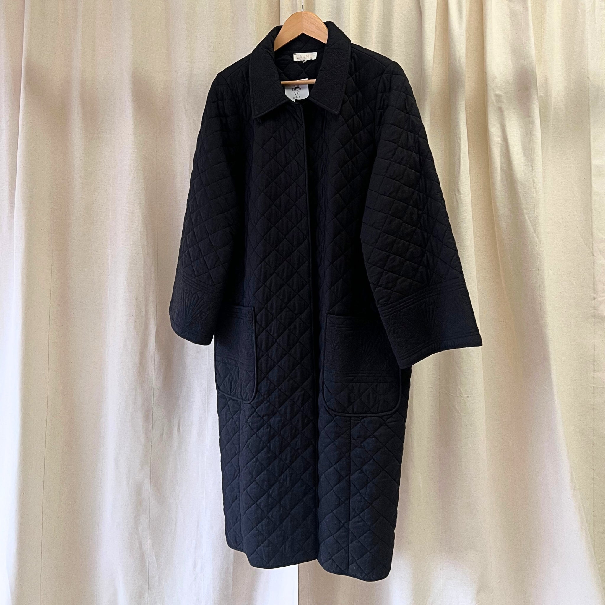 Black quilted coat on a hanger against a beige curtain background