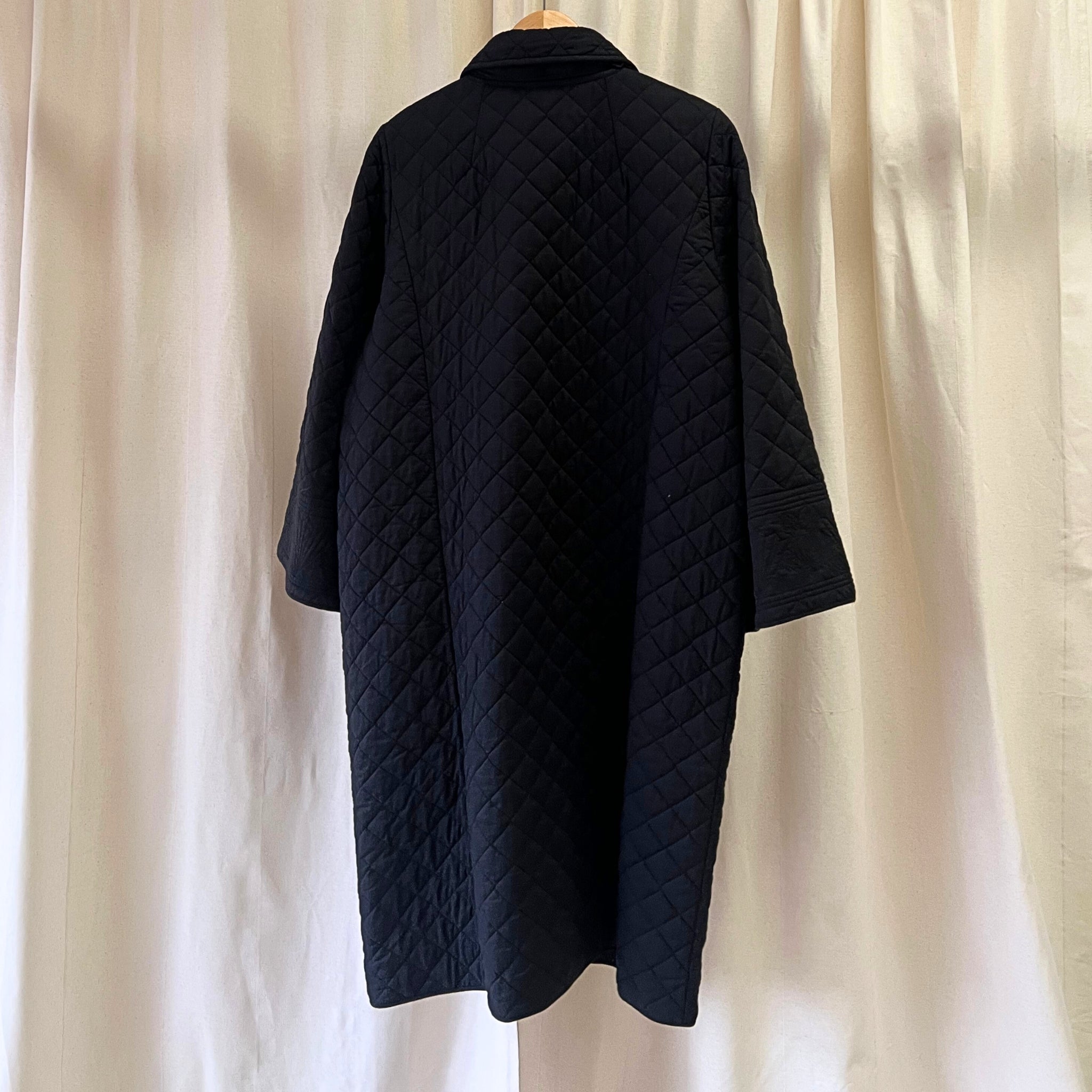 Black quilted coat on a mannequin against a beige curtain background