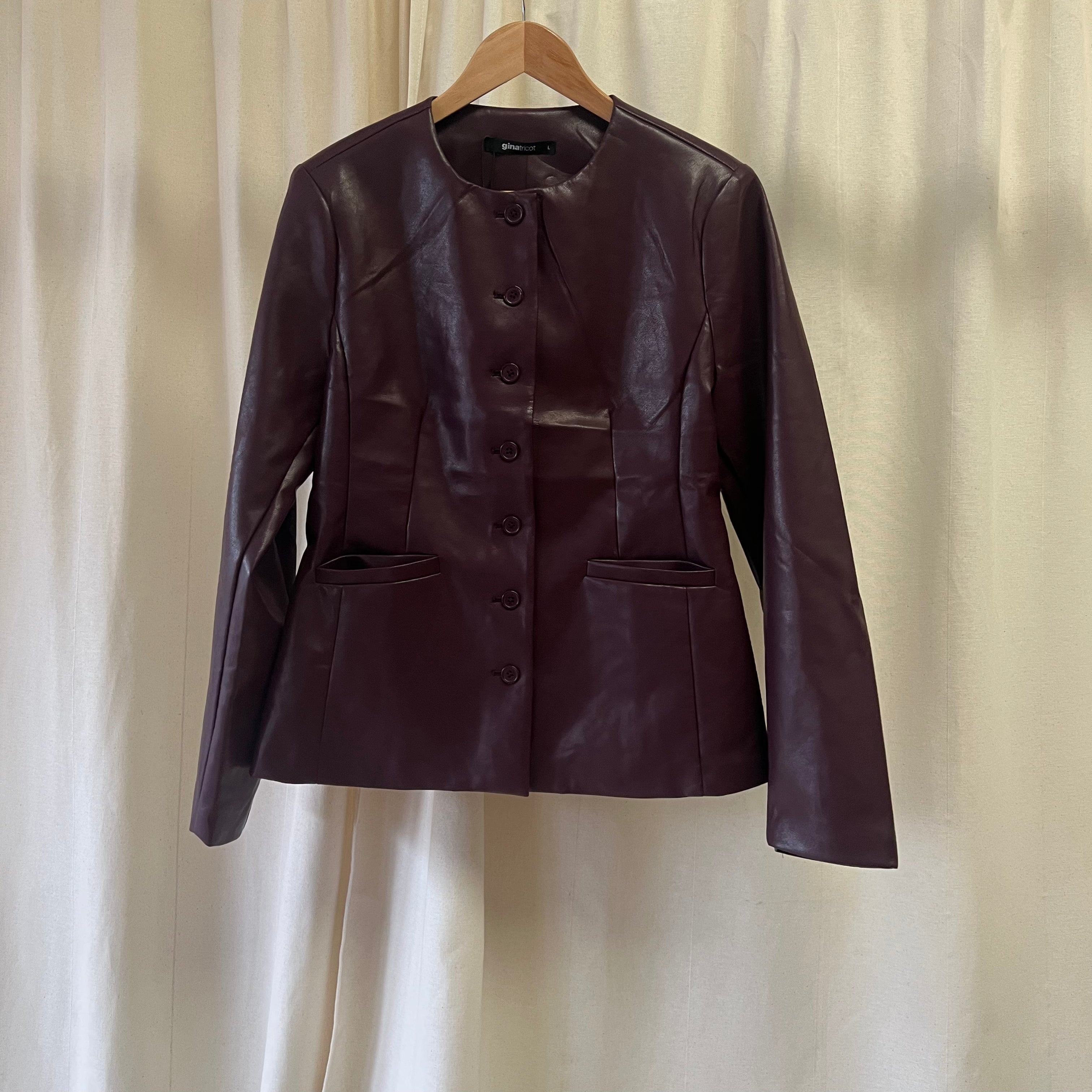 Brown leather jacket on a hanger against a beige curtain background