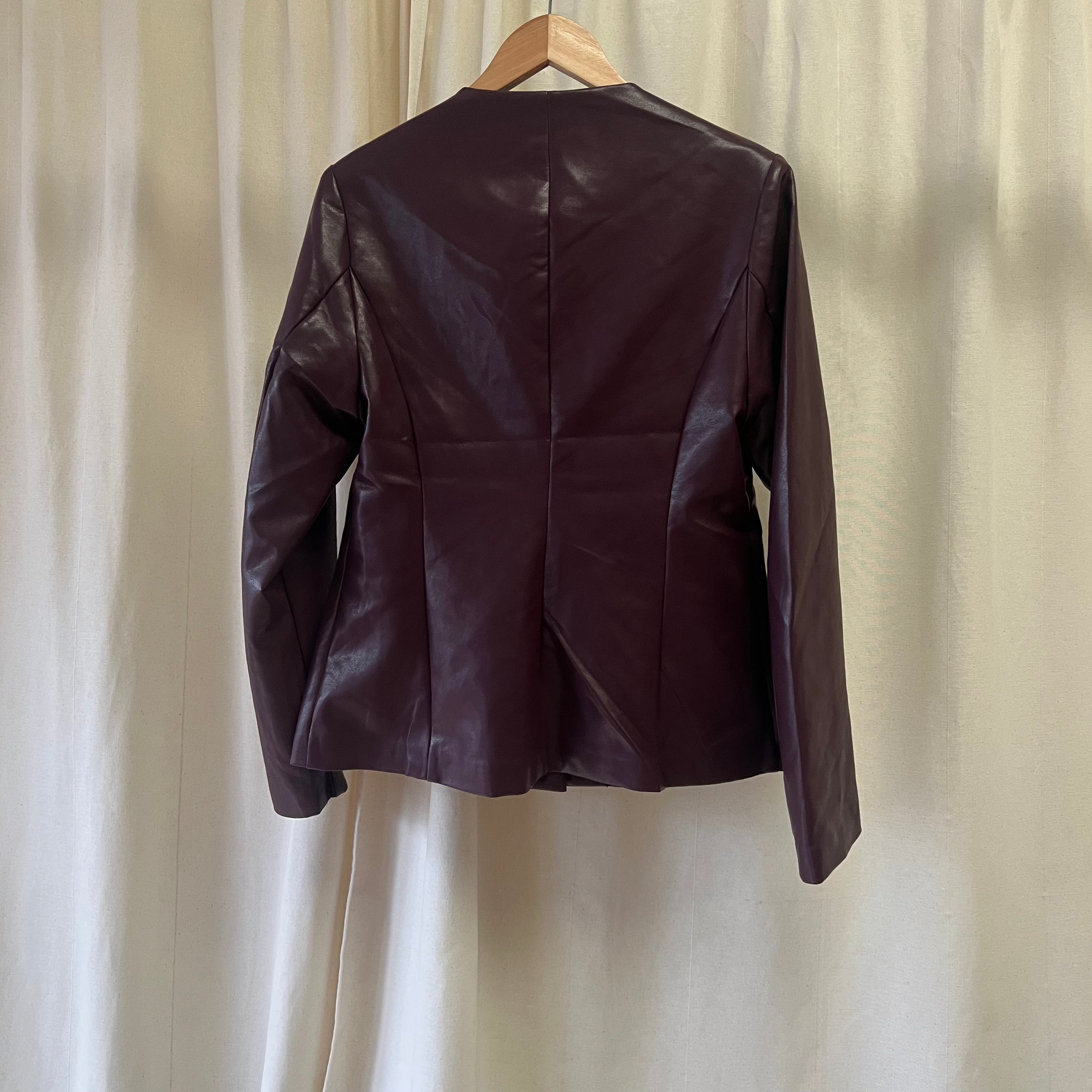 Brown leather jacket on a hanger against a beige curtain background