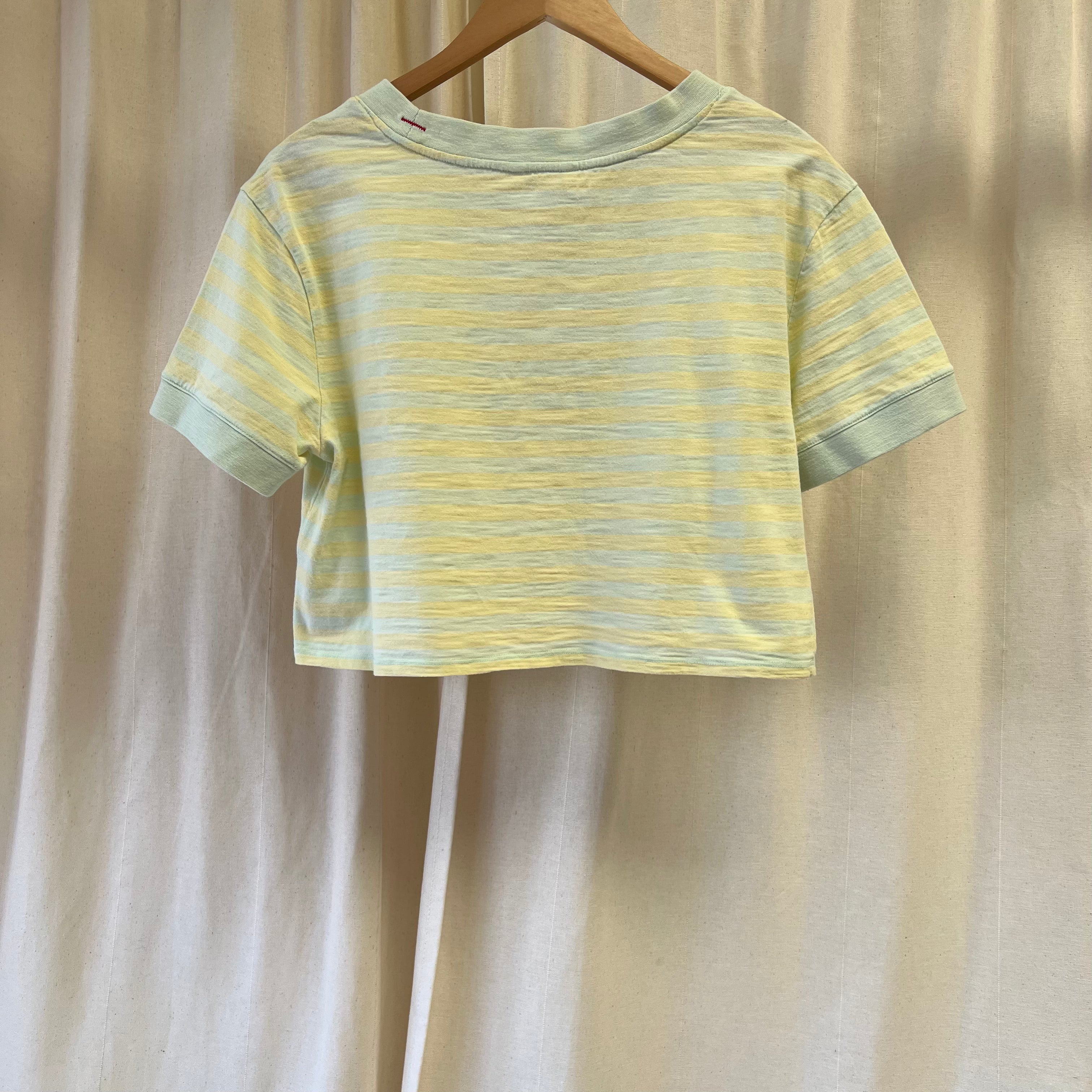 Yellow and green striped t-shirt on a wooden hanger against a beige curtain background