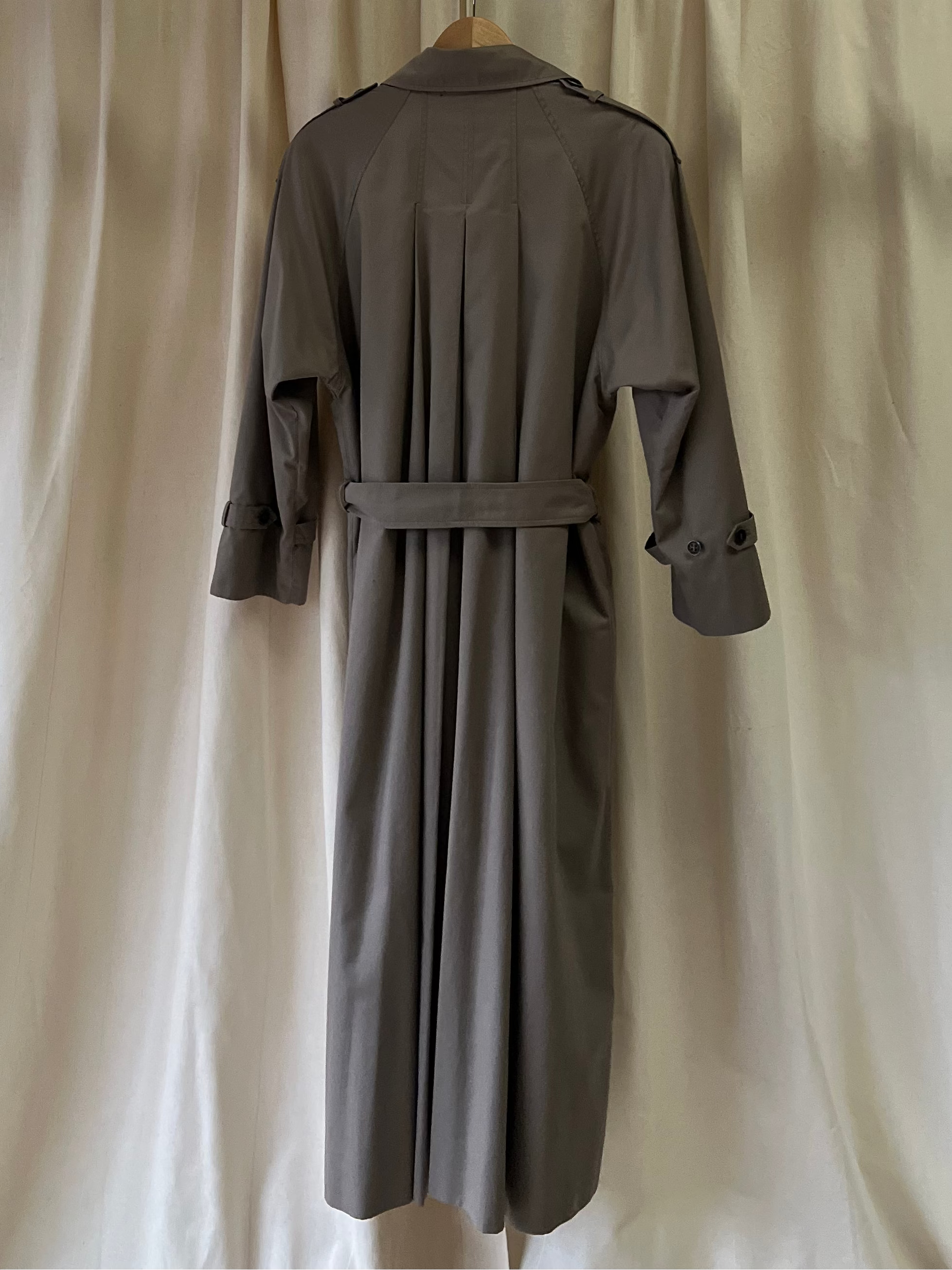 Grey coat hanging on a rod against a white curtain background