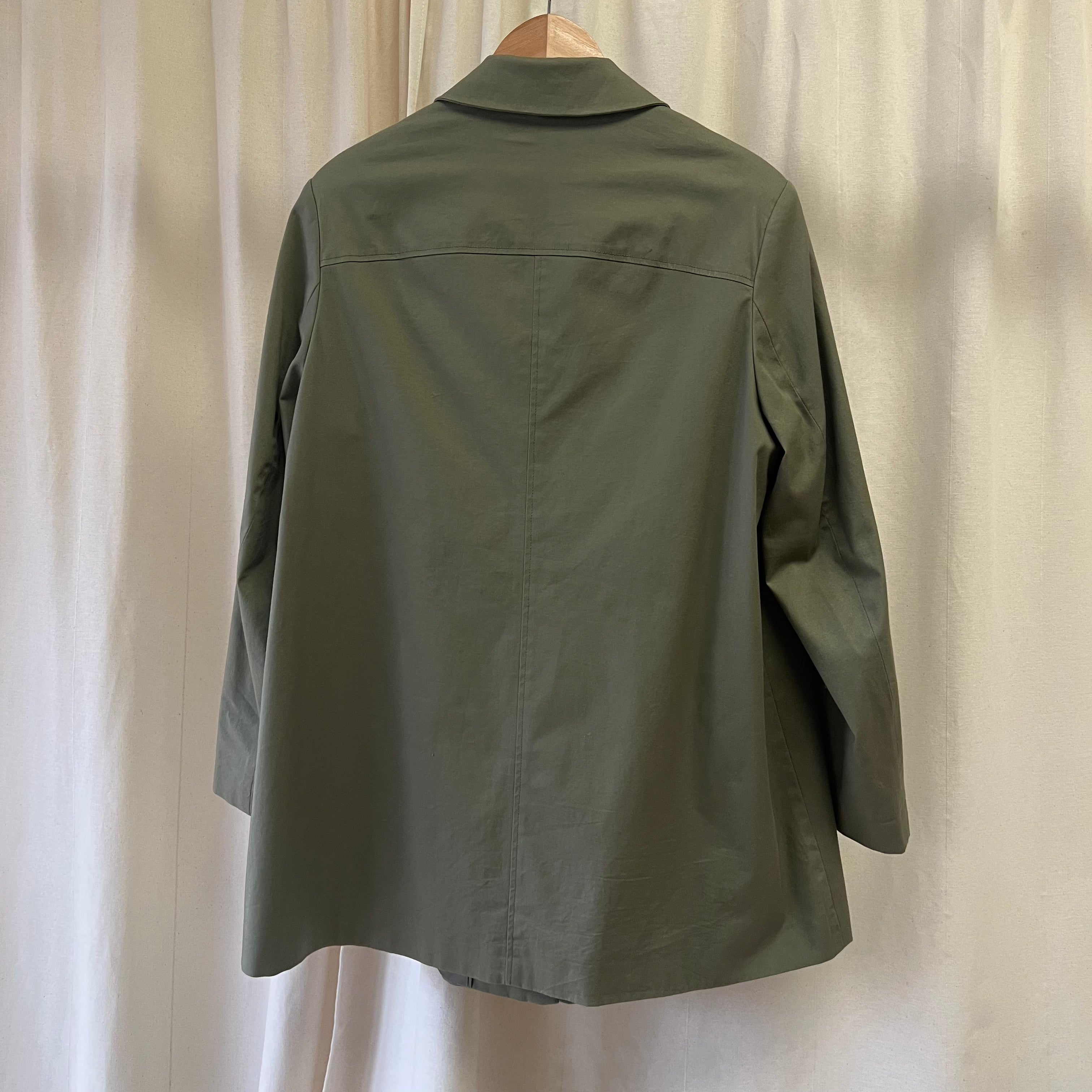 Green jacket on a hanger against a beige curtain background