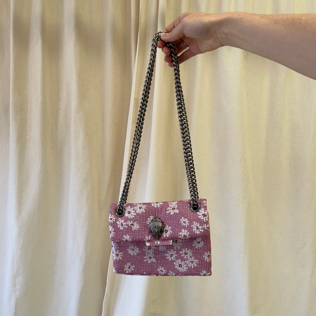 Hand holding a pink floral handbag with a chain strap against a beige curtain background
