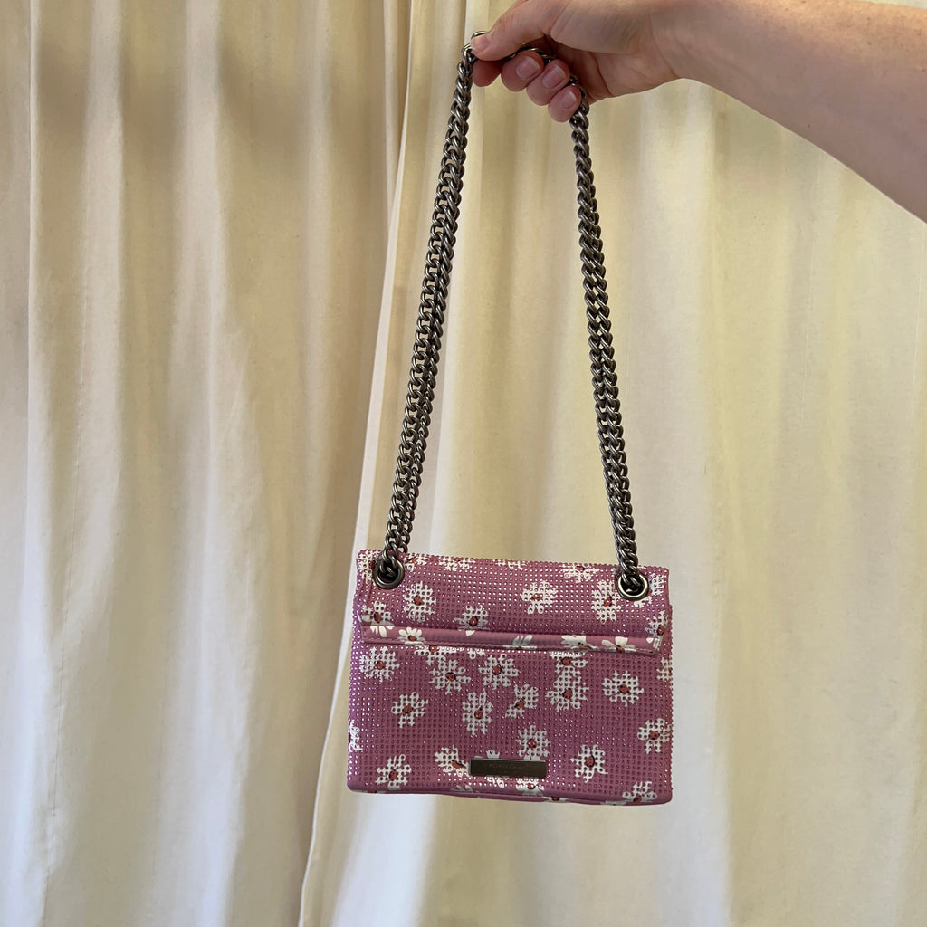 Hand holding a pink floral handbag with a chain strap against a beige curtain background