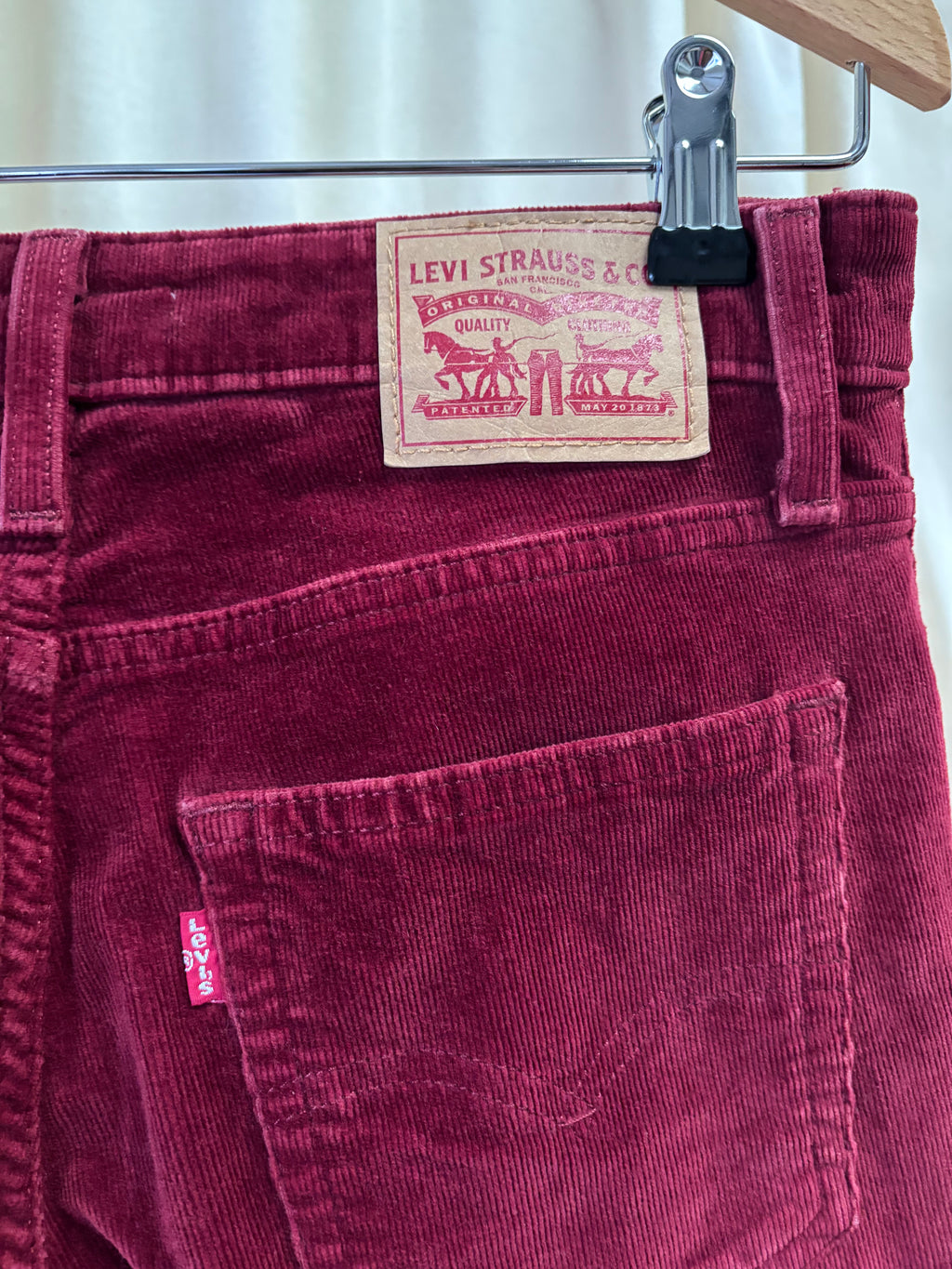 Maroon Levi's corduroy pants on a hanger with a visible tag.