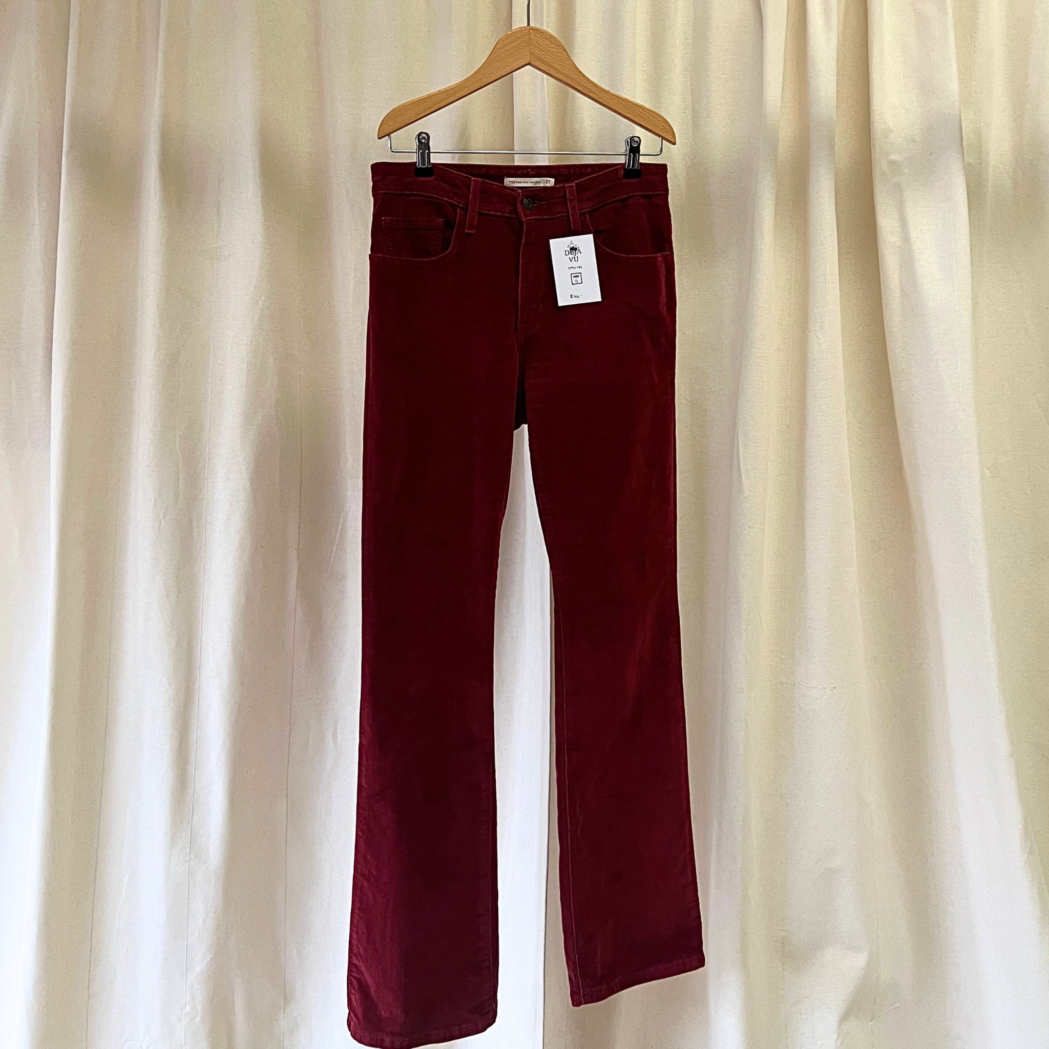 Maroon pants on a hanger against a beige curtain background