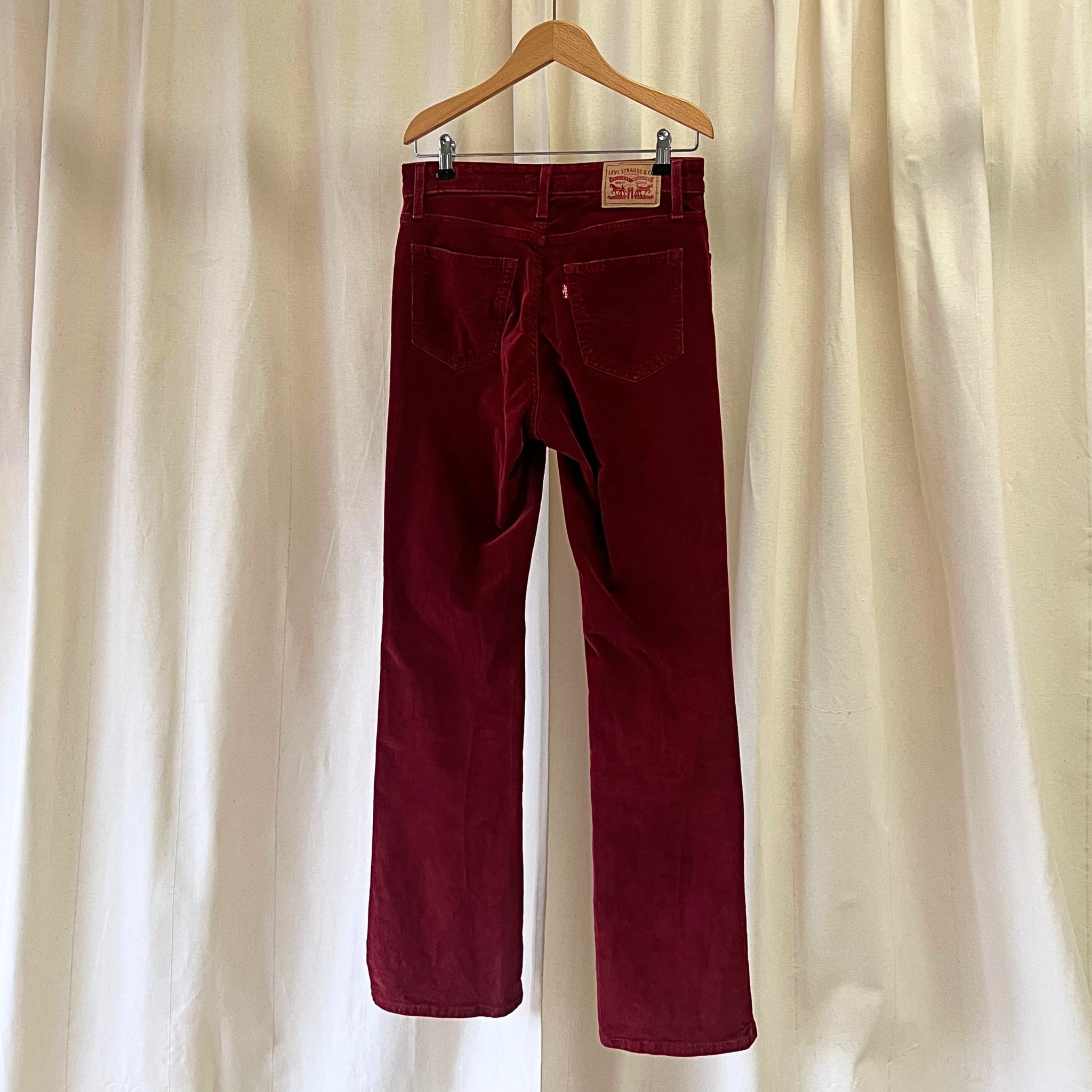 Maroon pants on a hanger against a beige curtain background