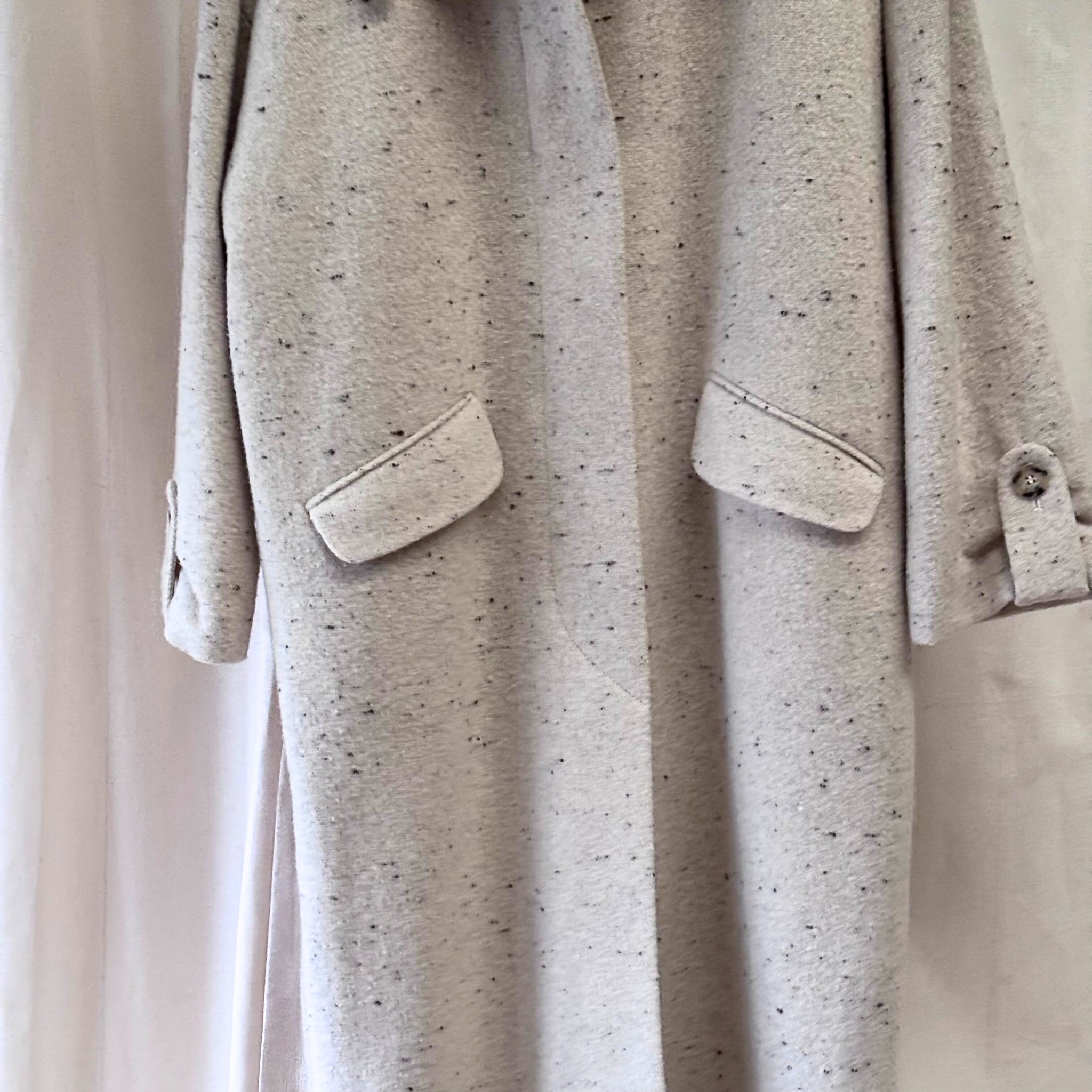 Close-up of a light gray textured coat with pockets on a neutral background