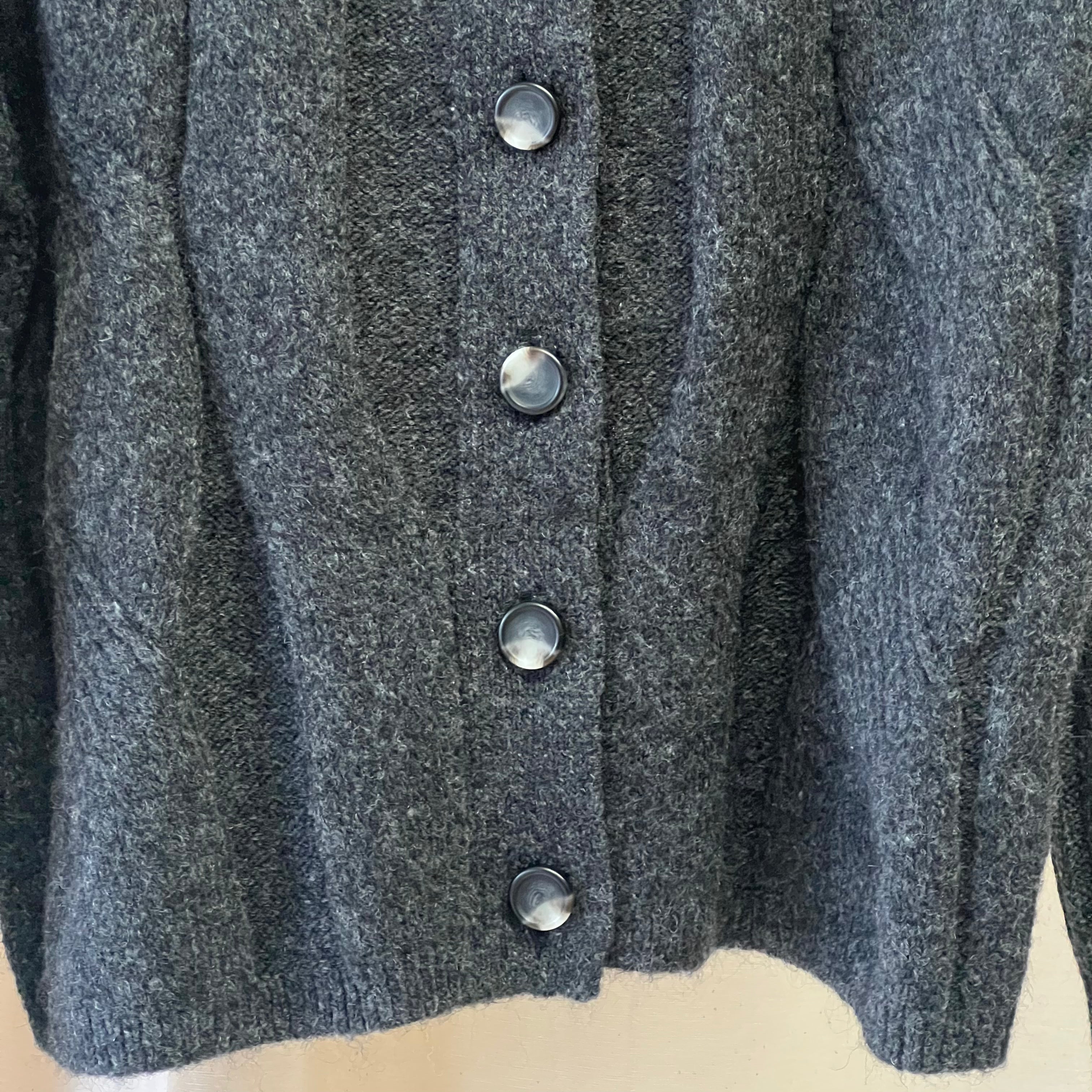 Close-up of a gray cardigan with buttons on a beige surface